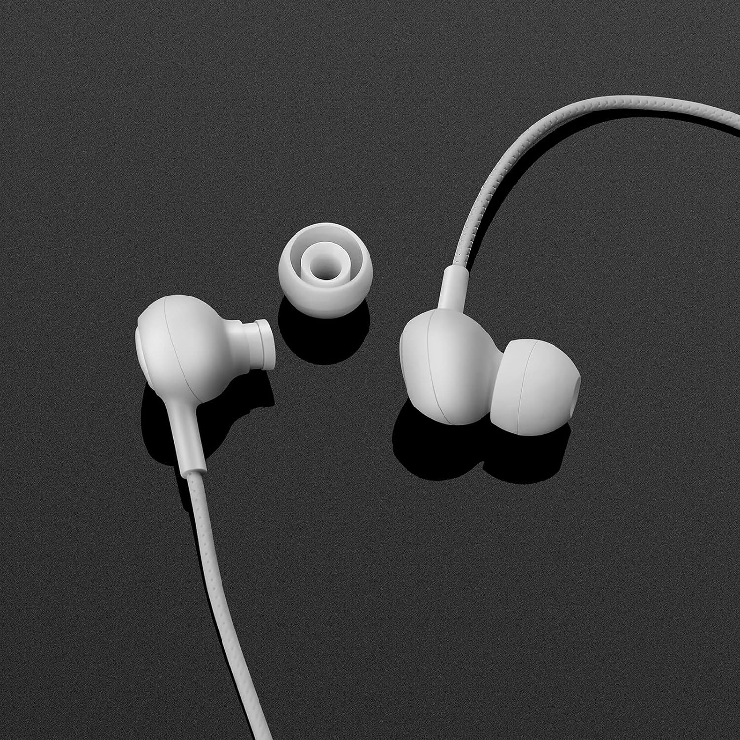 Weiße Ohrhörer mit Kabel und Ersatzspitzen auf schwarzem Hintergrund.