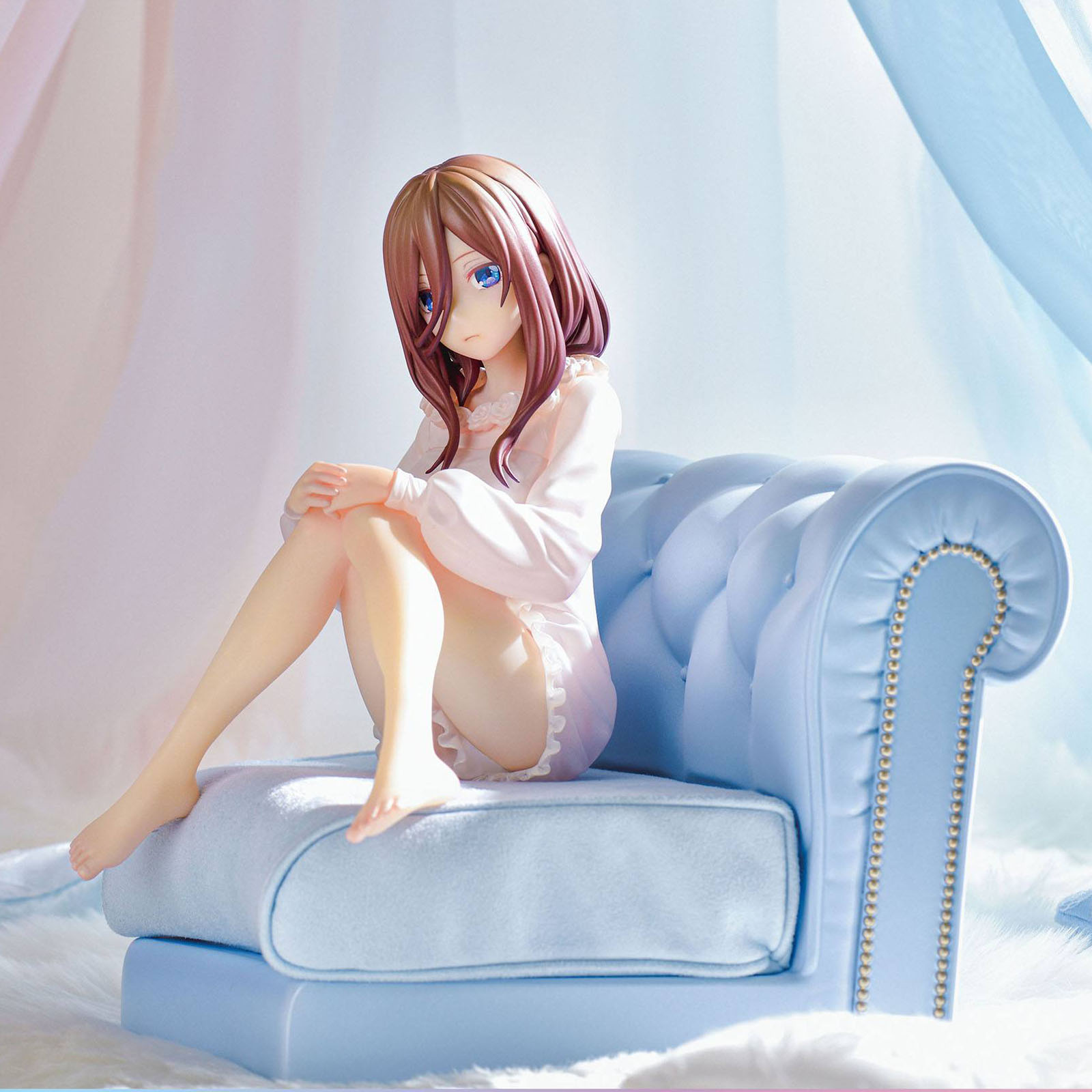 Anime-Figur eines Mädchens in rosa Nachtwäsche auf einem hellblauen Sofa.