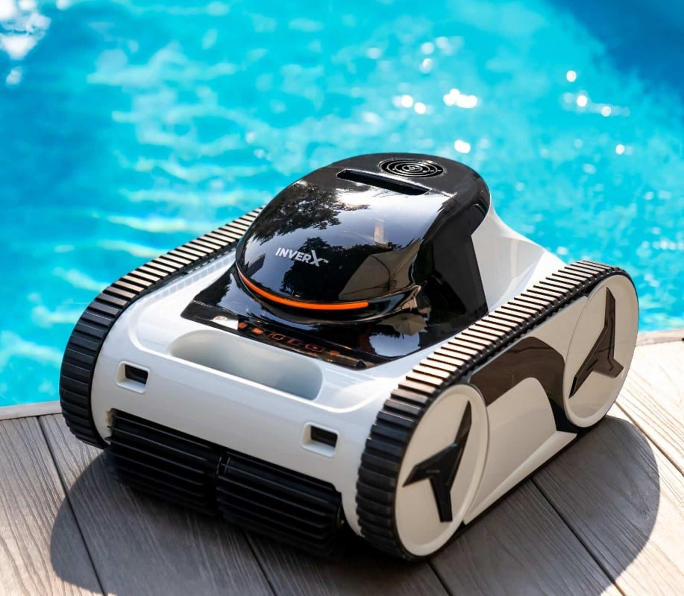 Un robot limpiafondos blanco con orugas negras está sobre una terraza de madera junto a una piscina azul.