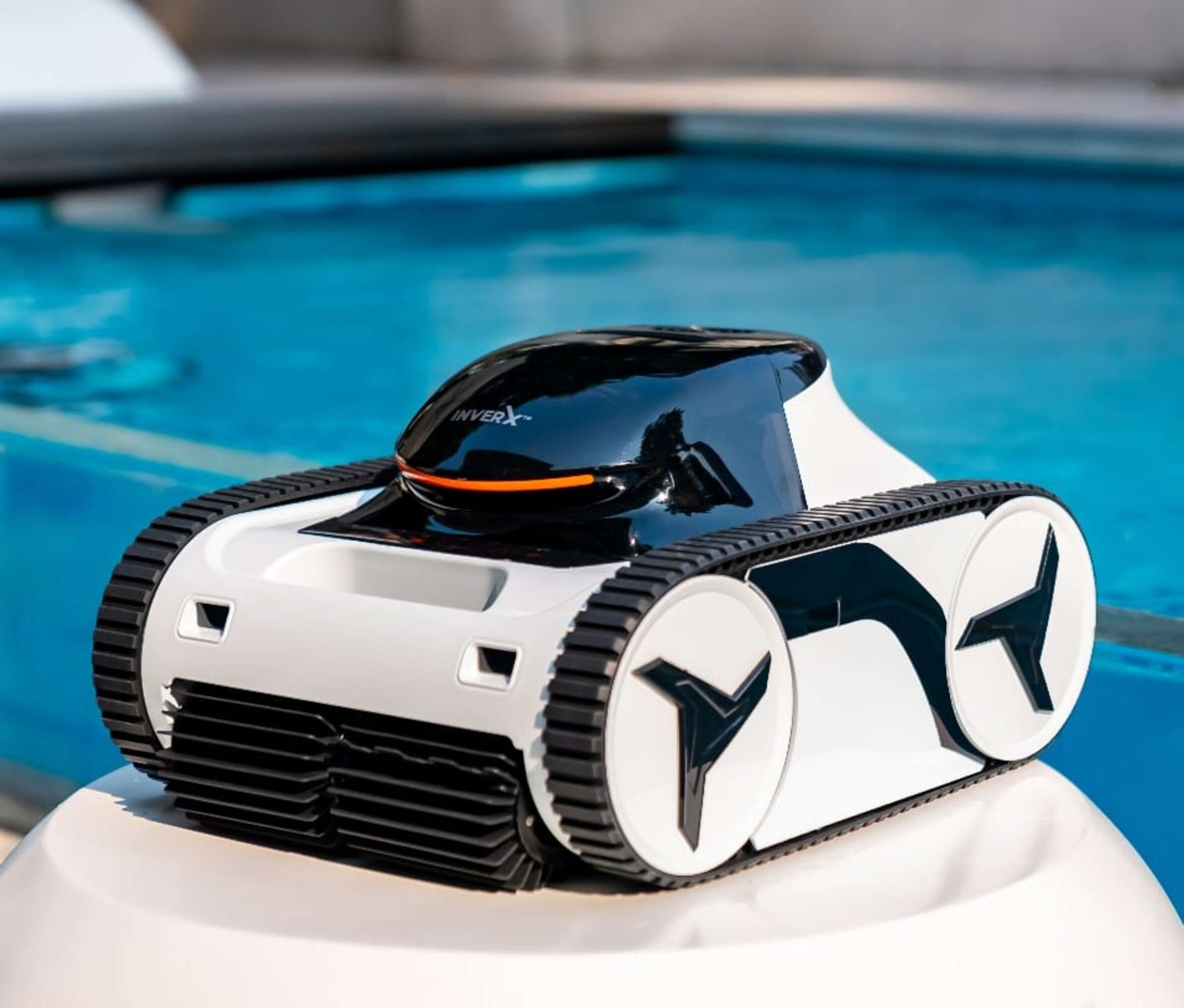 Un robot de piscina blanco y negro se sienta en una plataforma blanca junto a una piscina azul.