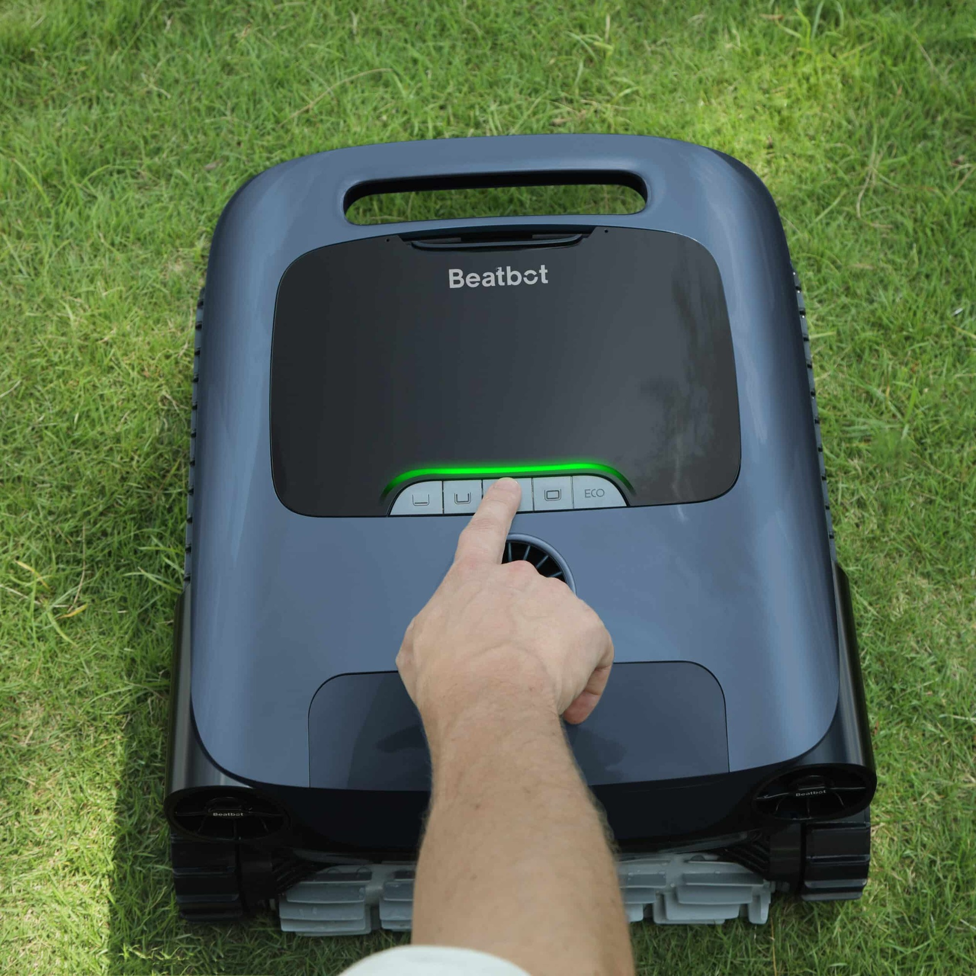 Ein Finger drückt eine Taste auf einem grauen Beatbot-Rasenmähroboter im Gras.
