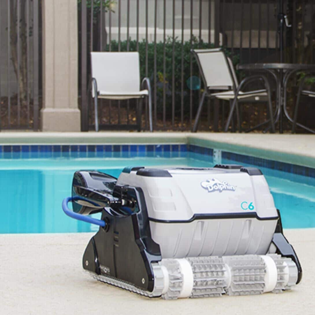 Un limpiador de piscinas Dolphin C6 está al borde junto a una piscina azul.
