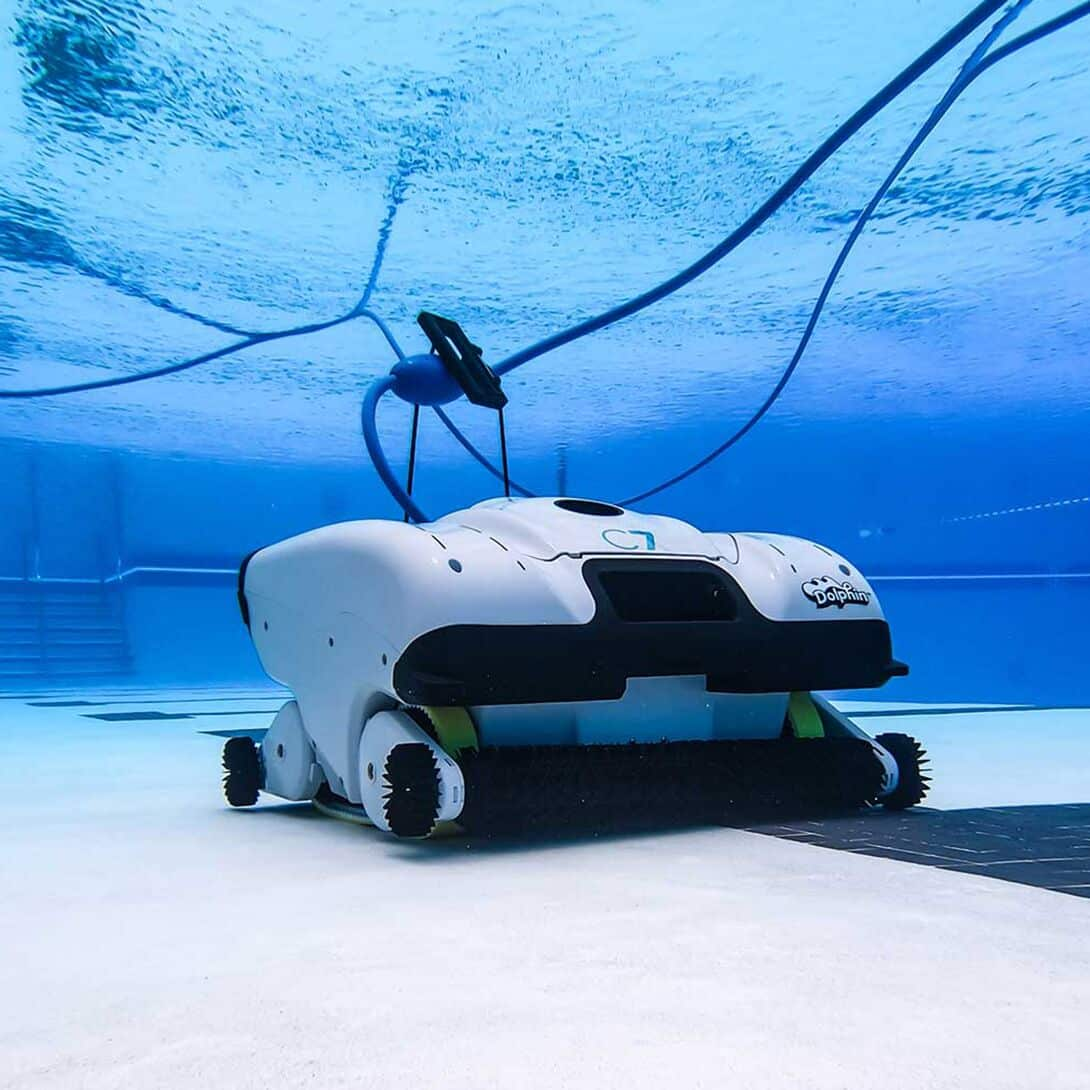Un robot limpiador blanco con mango negro se mueve por el fondo de la piscina.