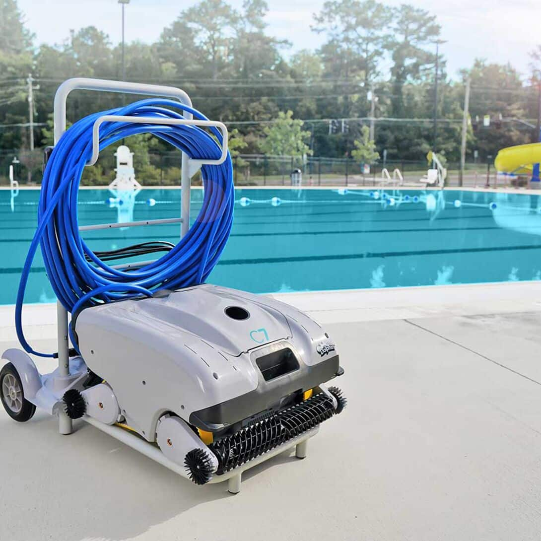Un limpiador de piscinas está junto a una piscina con una manguera azul enrollada en un carro.