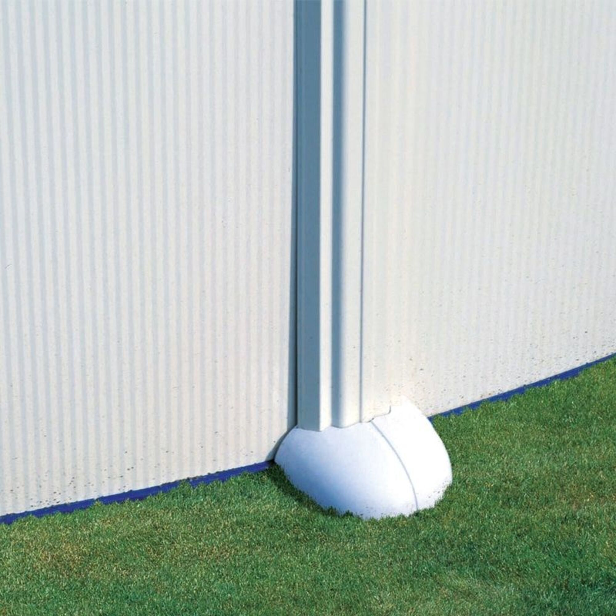 Soporte blanco con borde azul sobre césped verde contra pared vertical.