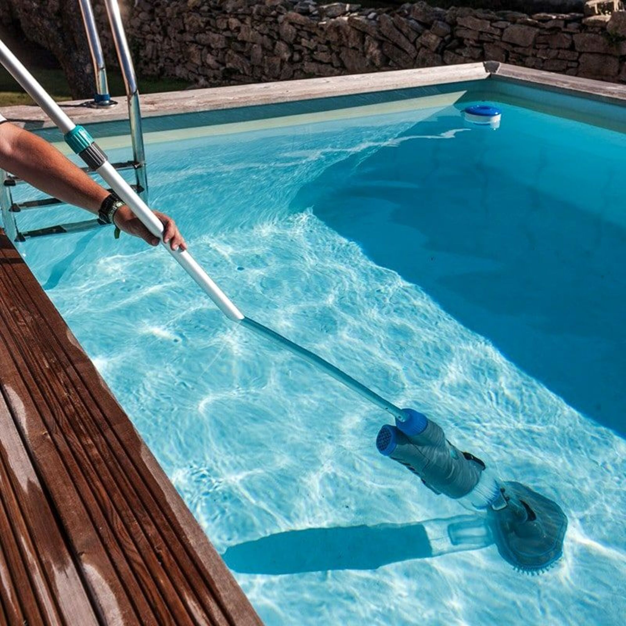 Una mano usa un limpiafondos en el agua azul de una piscina.