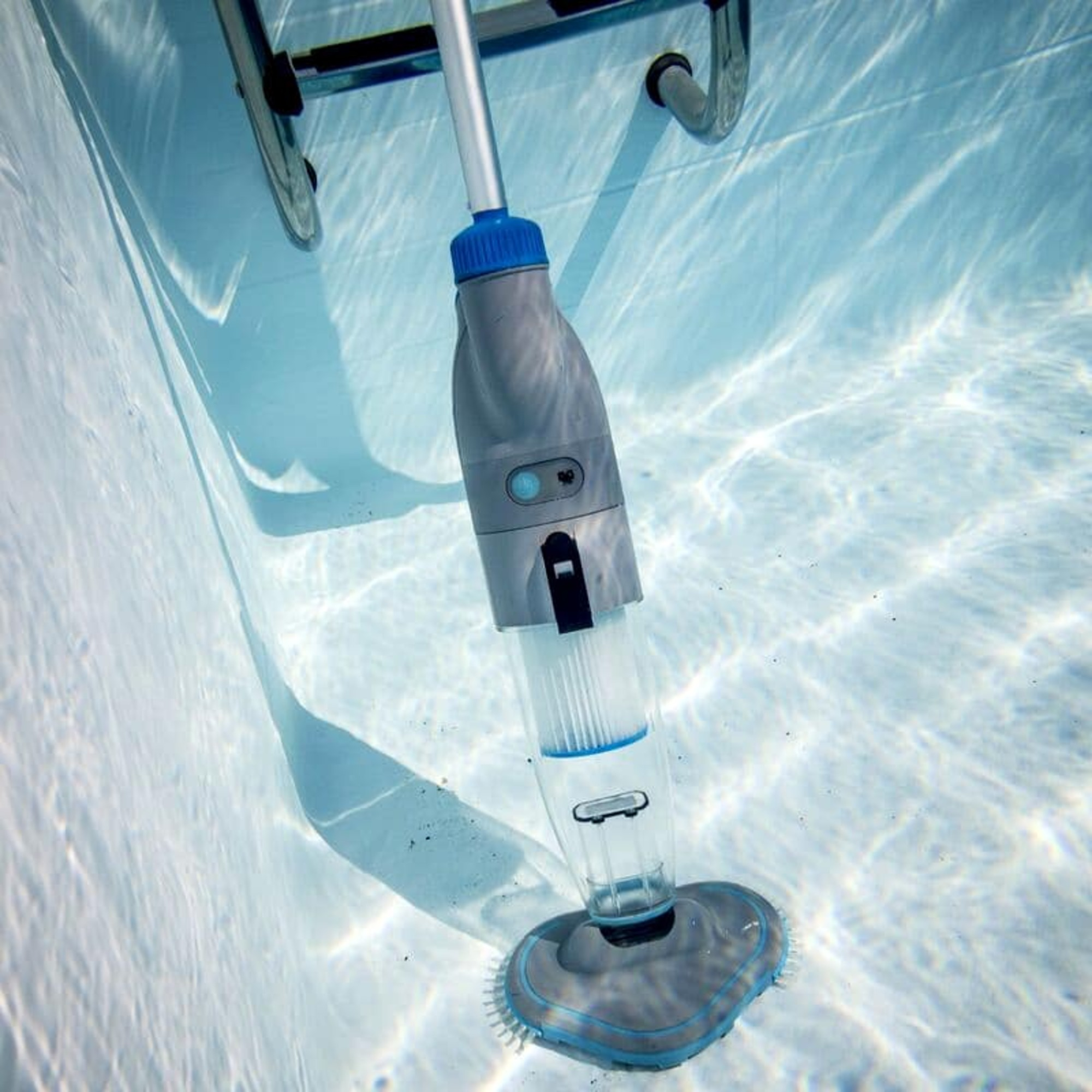 Limpiafondos de piscina submarino con mango azul y depósito transparente en suelo azul claro.