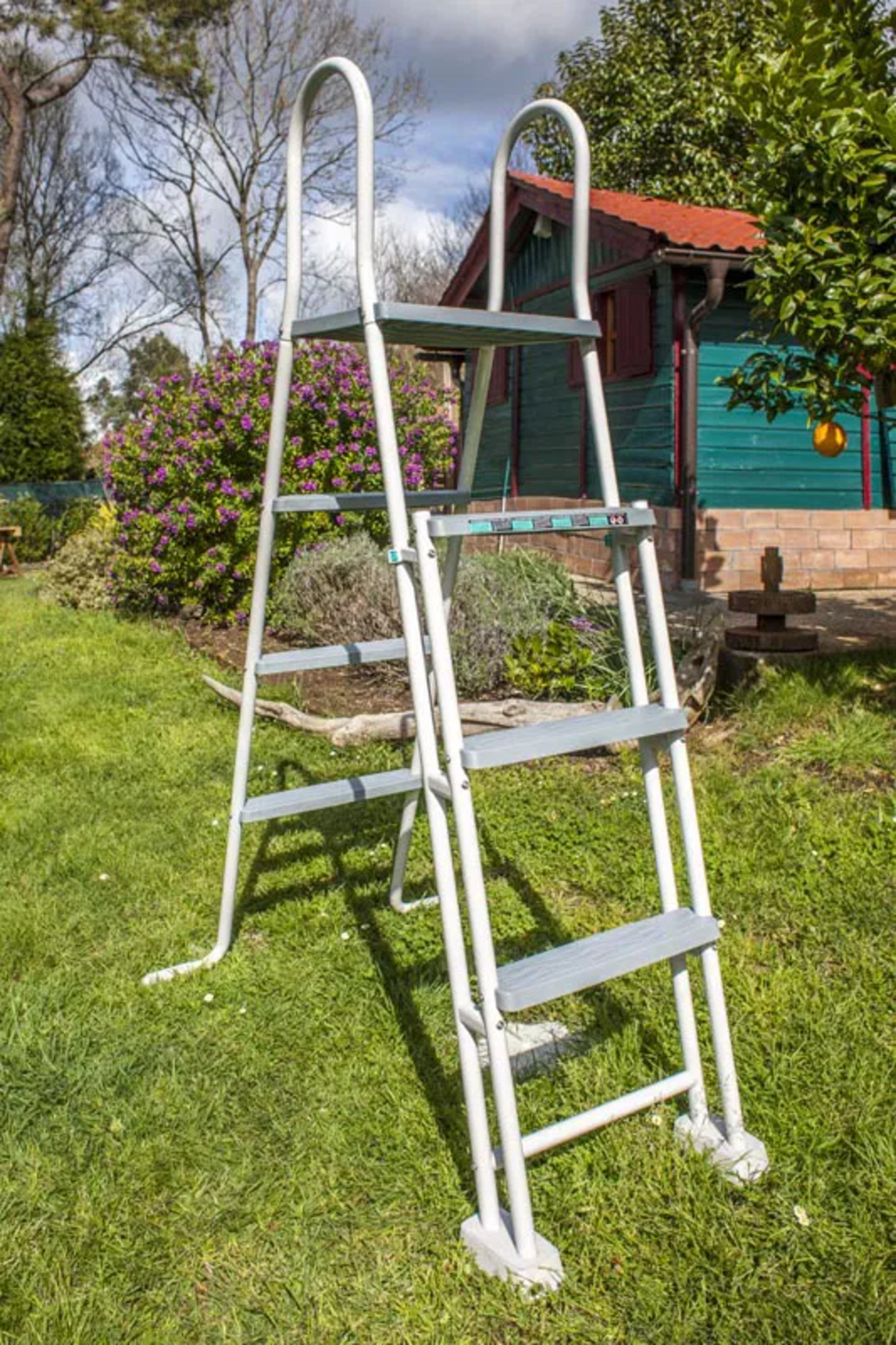 Una escalera blanca sobre hierba verde delante de una casita de madera.