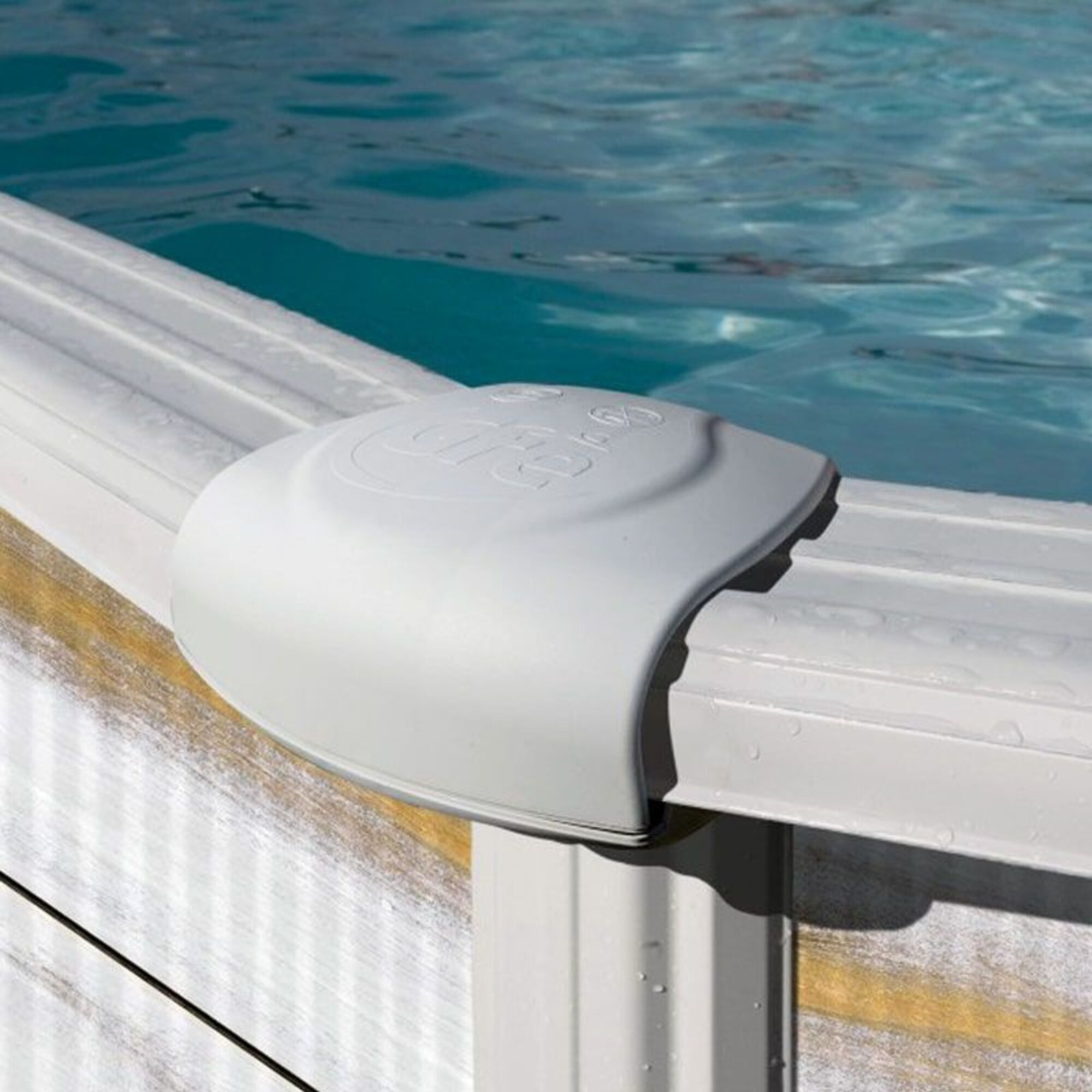 Cubierta de esquina de piscina gris sobre agua azul y borde blanco.