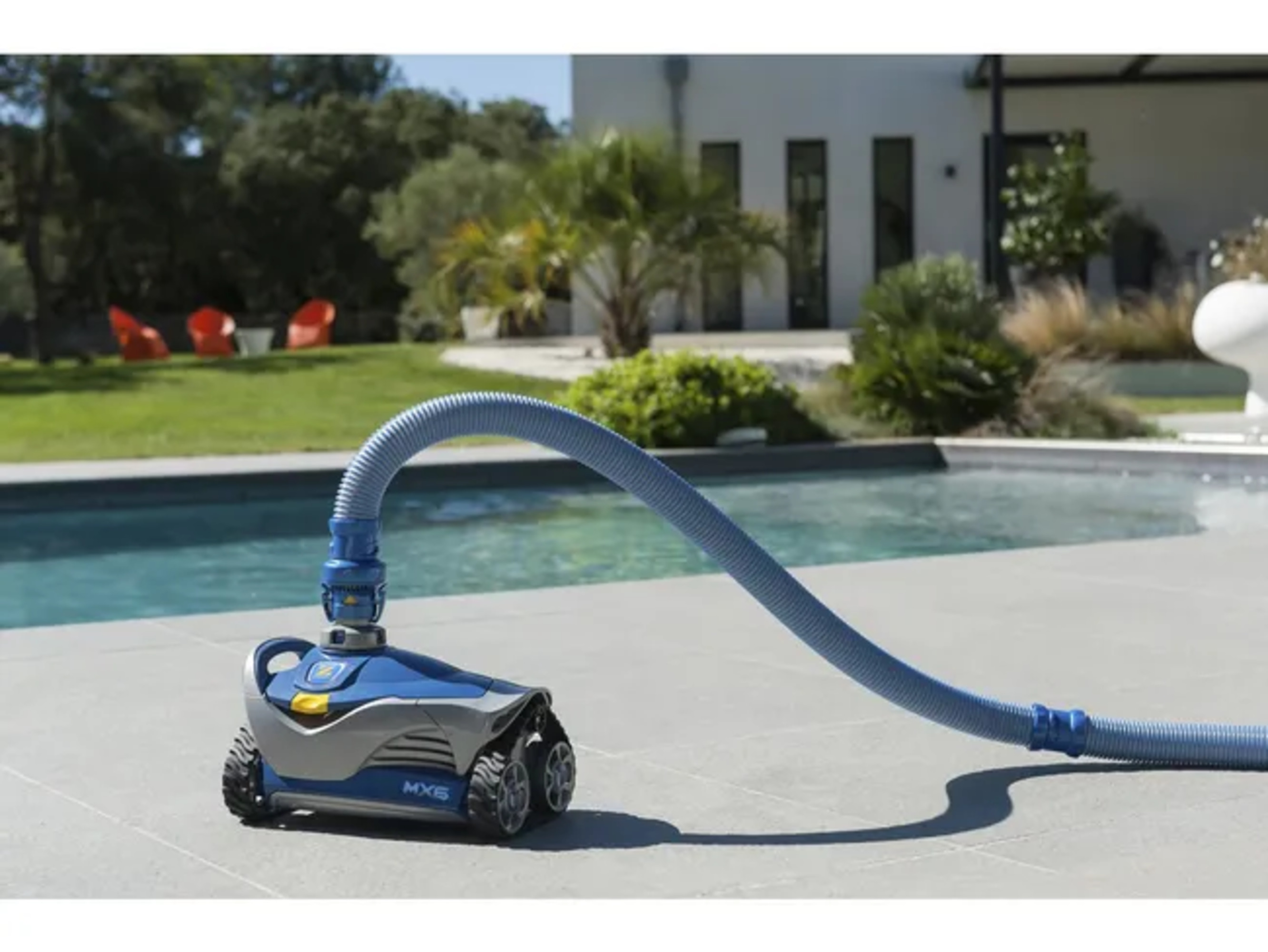 Ein blauer Poolreiniger mit Schlauch am Beckenrand auf einer Terrasse.