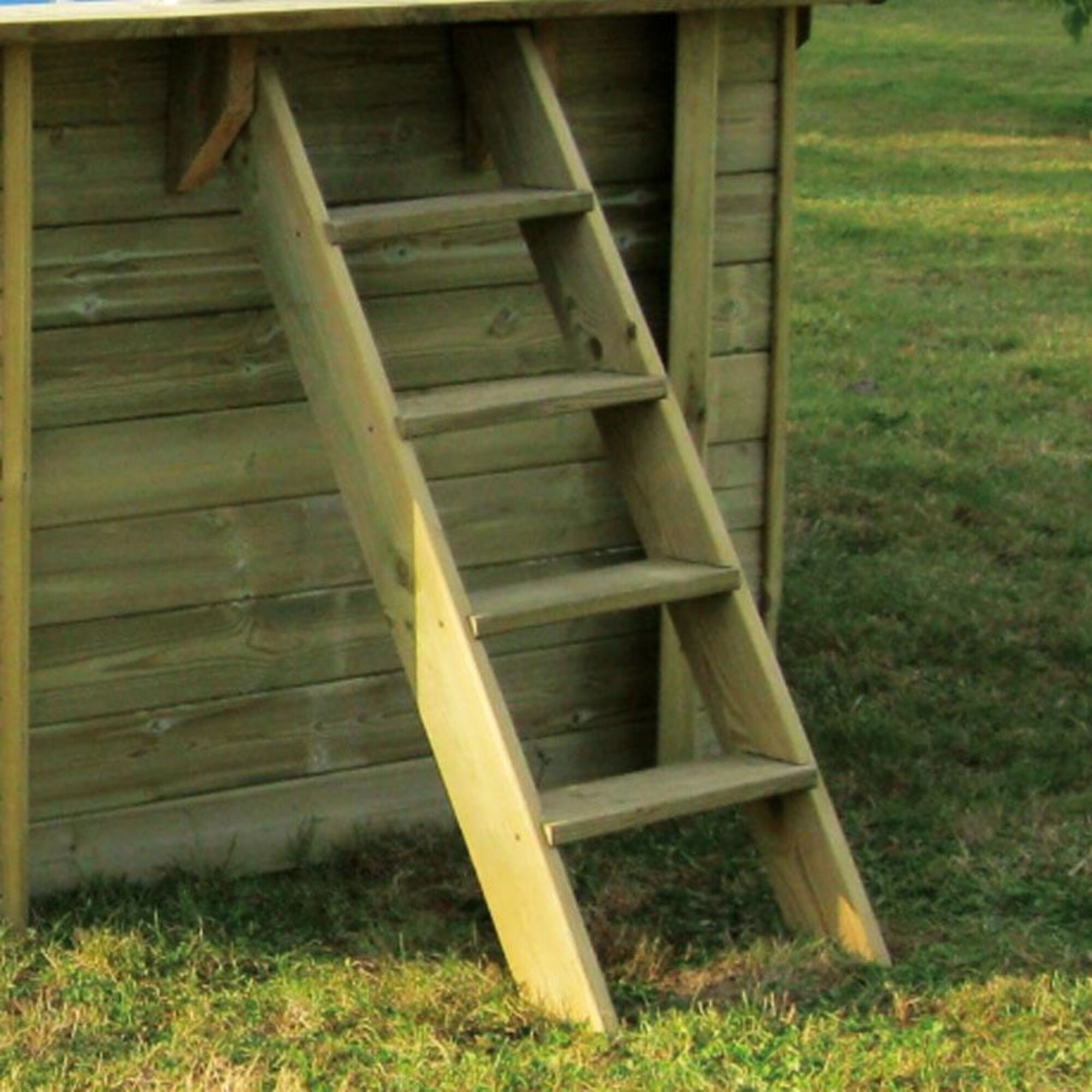 Una escalera de madera se apoya en una pared revestida de madera, con césped delante.