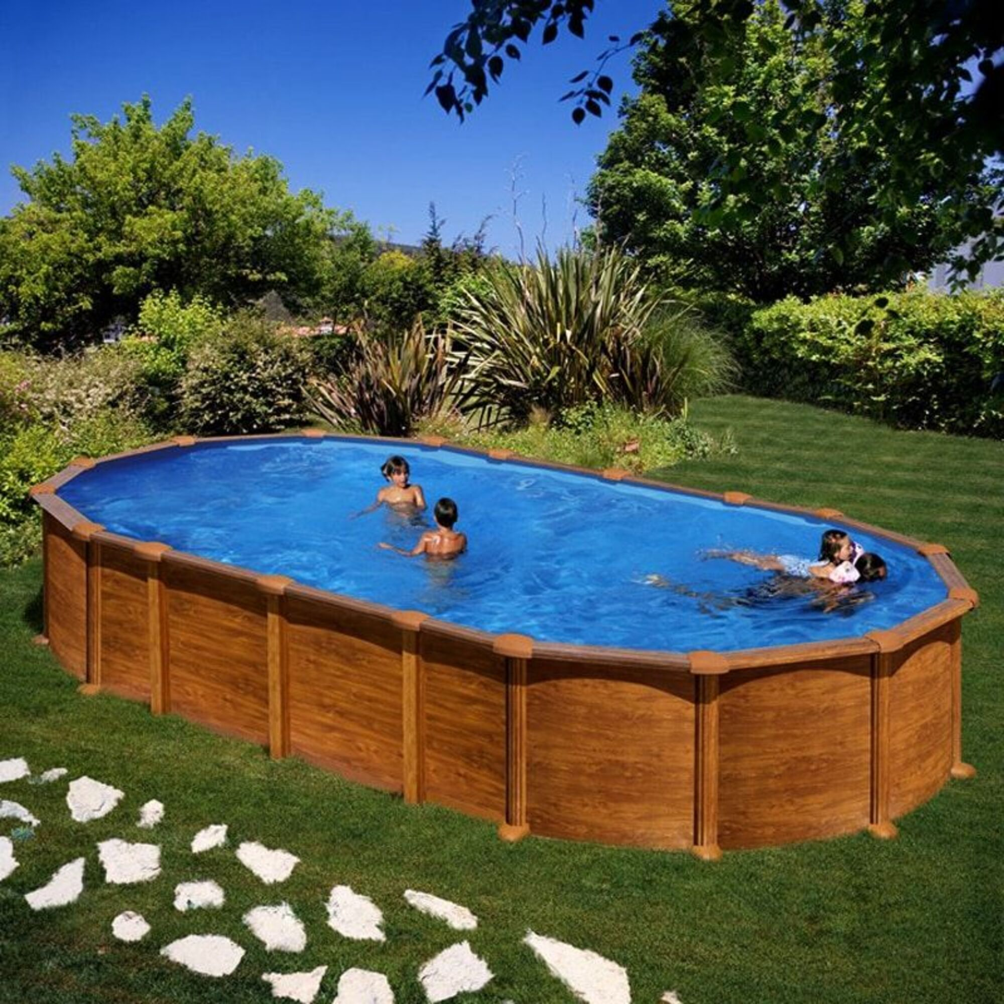 Los niños chapotean en una piscina ovalada de madera en un jardín soleado.