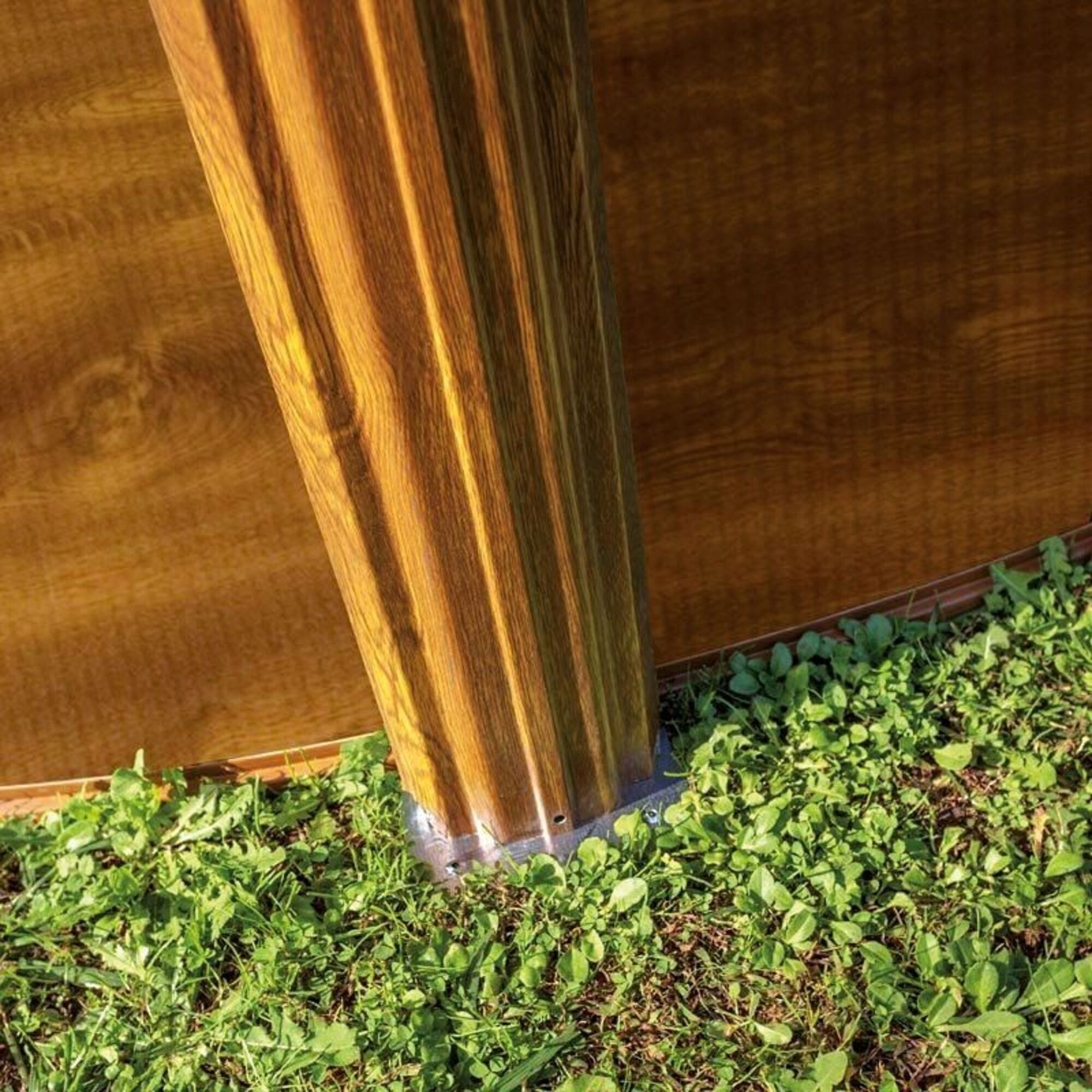 Poste de madera con ranuras verticales sobre césped. Fondo oscuro.