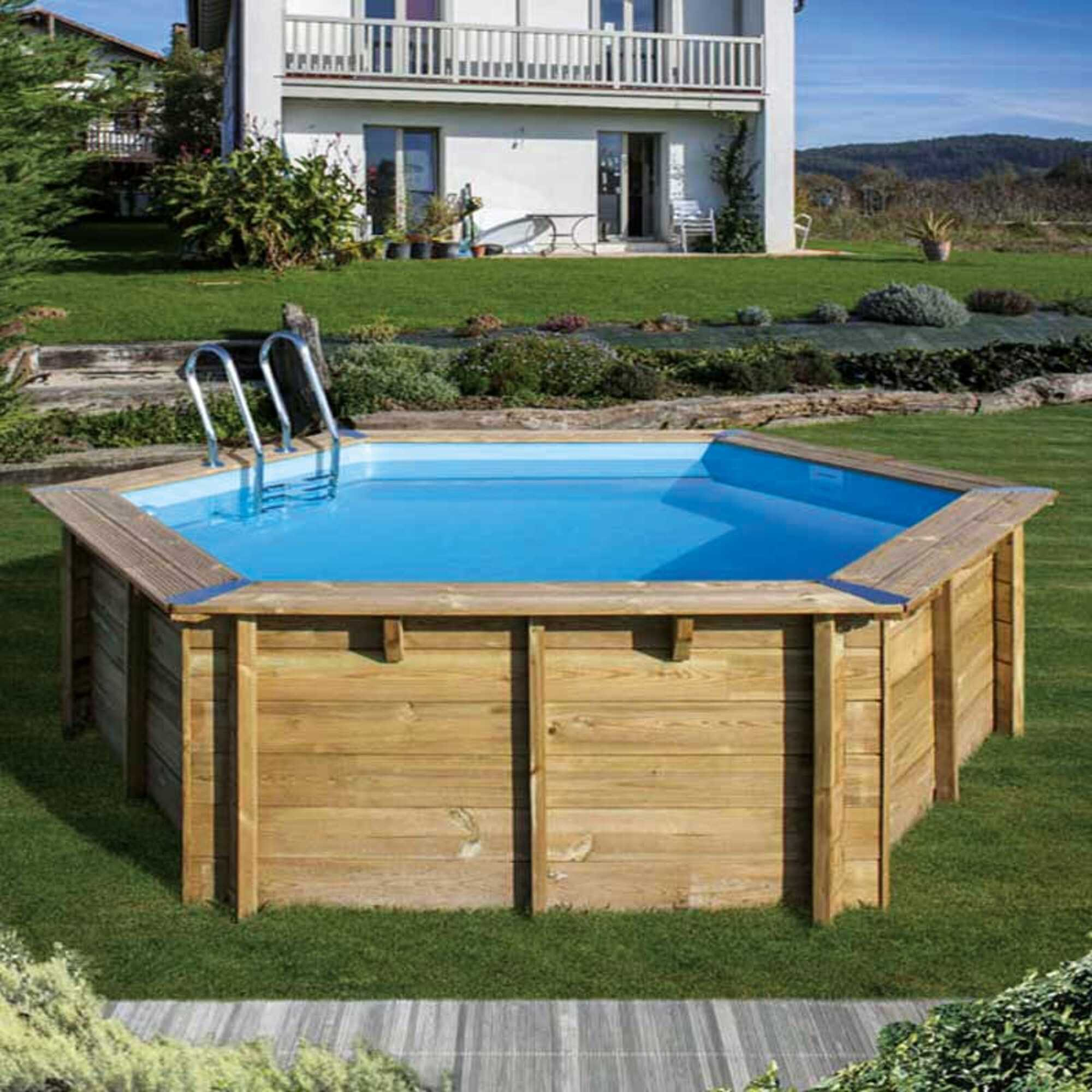Una piscina de madera con escalera se alza en un jardín frente a una casa.