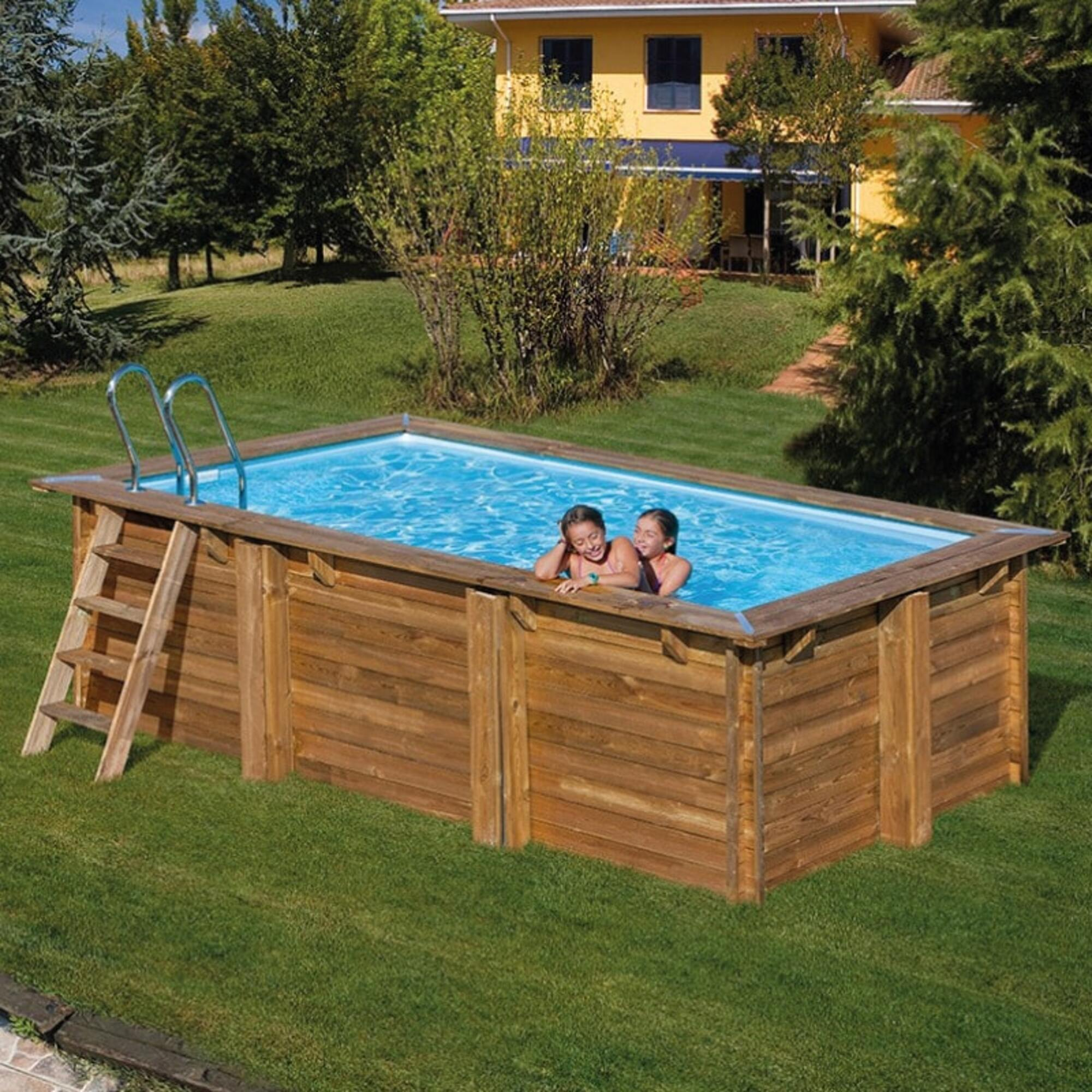 Dos niñas chapotean en una piscina de madera al aire libre. Se ven escalera y pasamanos.