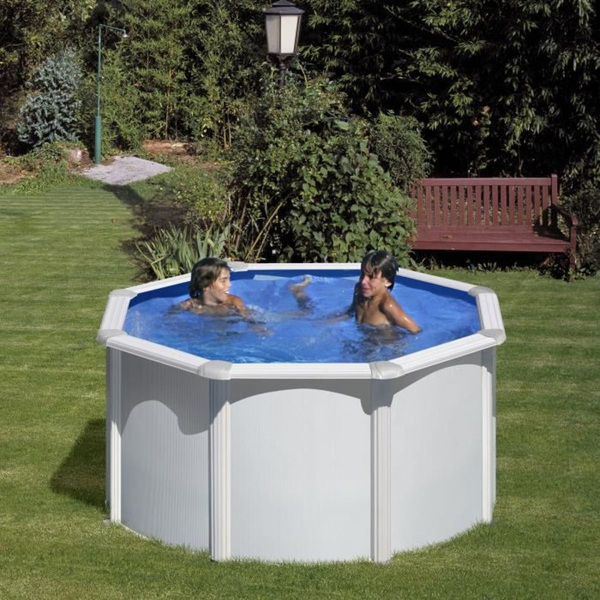 Dos niños chapotean en una piscina octogonal en un jardín. Un banco de madera al fondo.