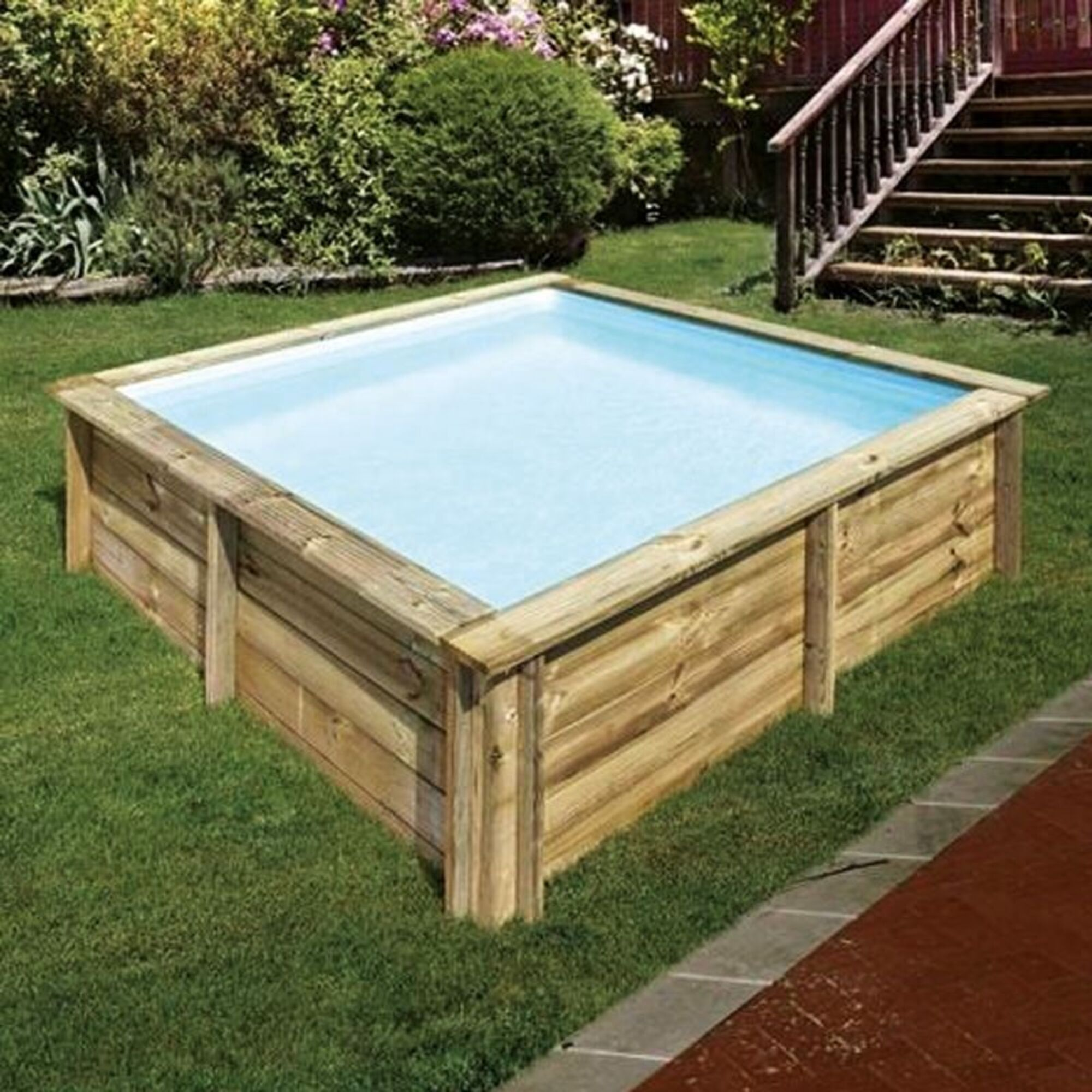 Una piscina cuadrada de madera con agua clara sobre césped verde.