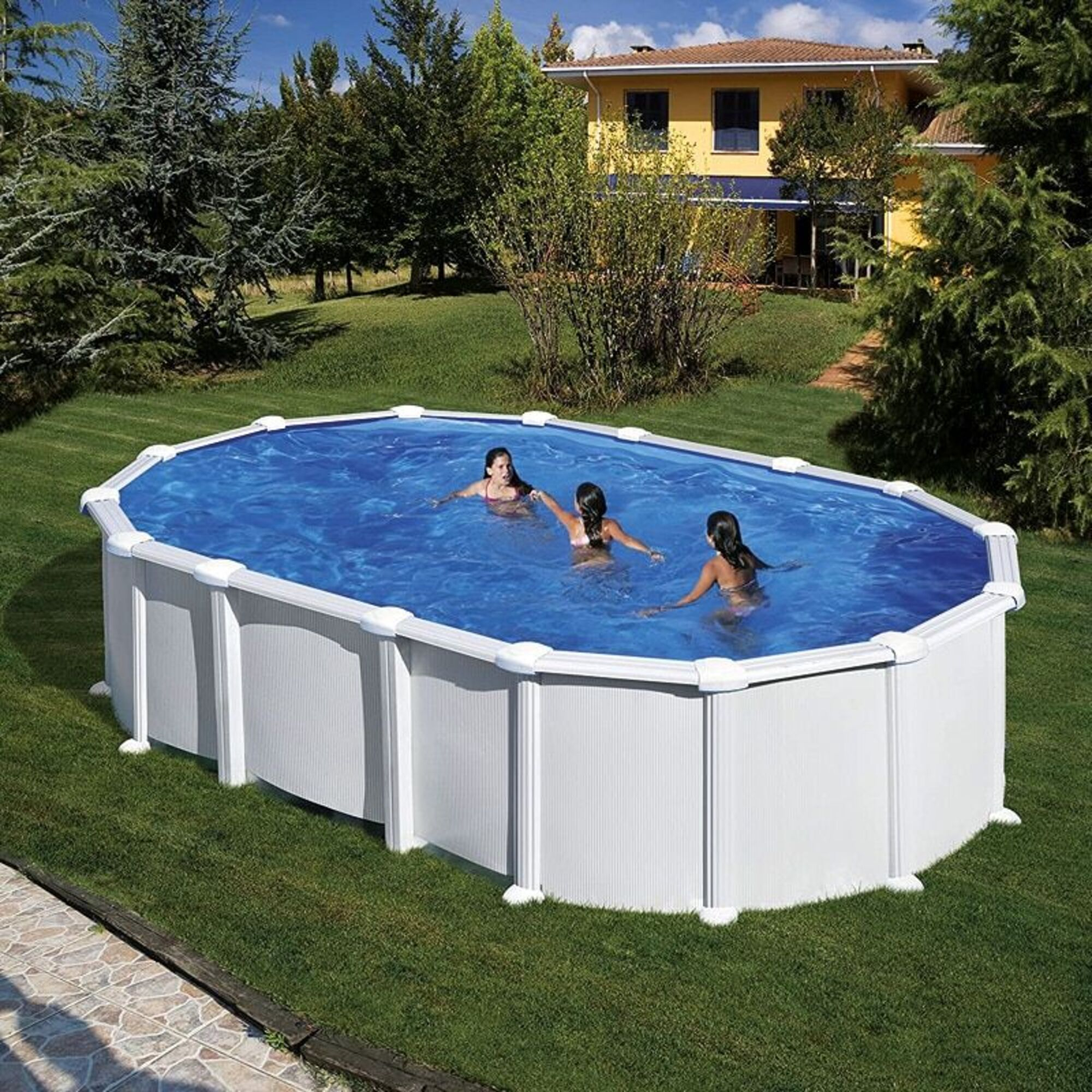 Tres chicas nadan en una piscina ovalada en un jardín. Una casa amarilla al fondo.