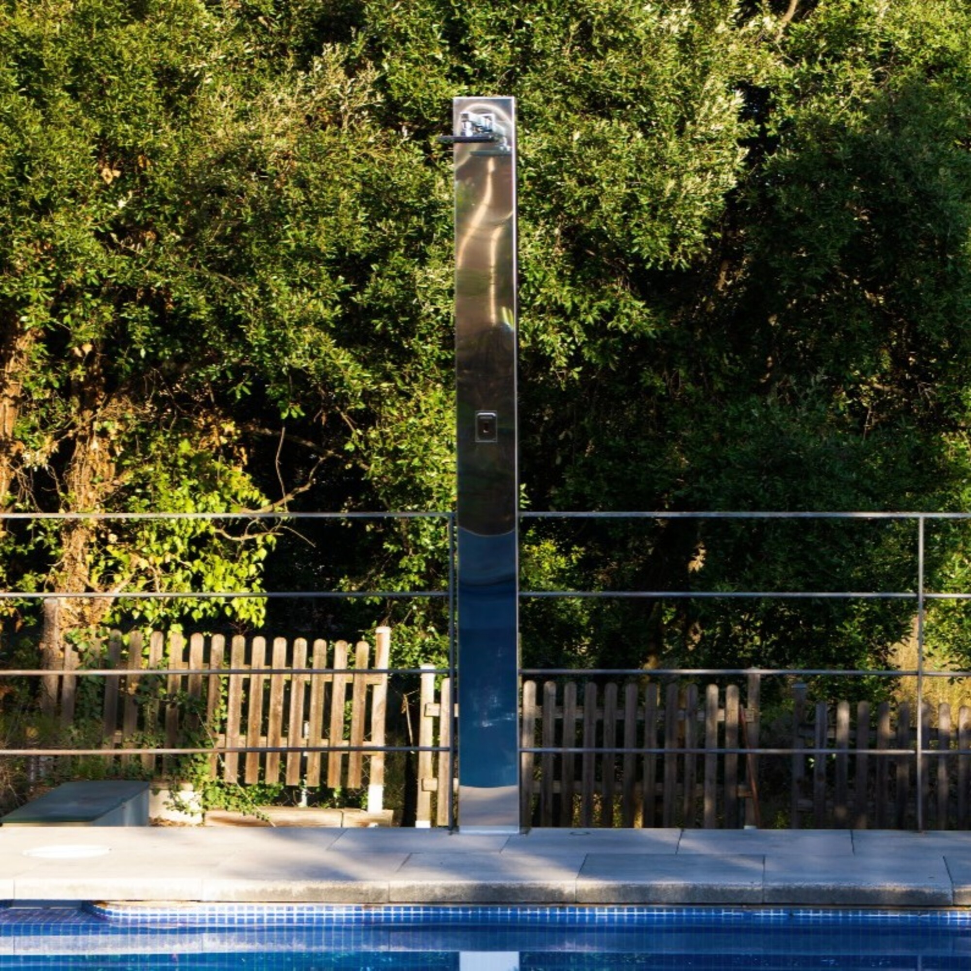 Una torre de ducha cromada moderna se encuentra junto a una piscina de baldosas azules.