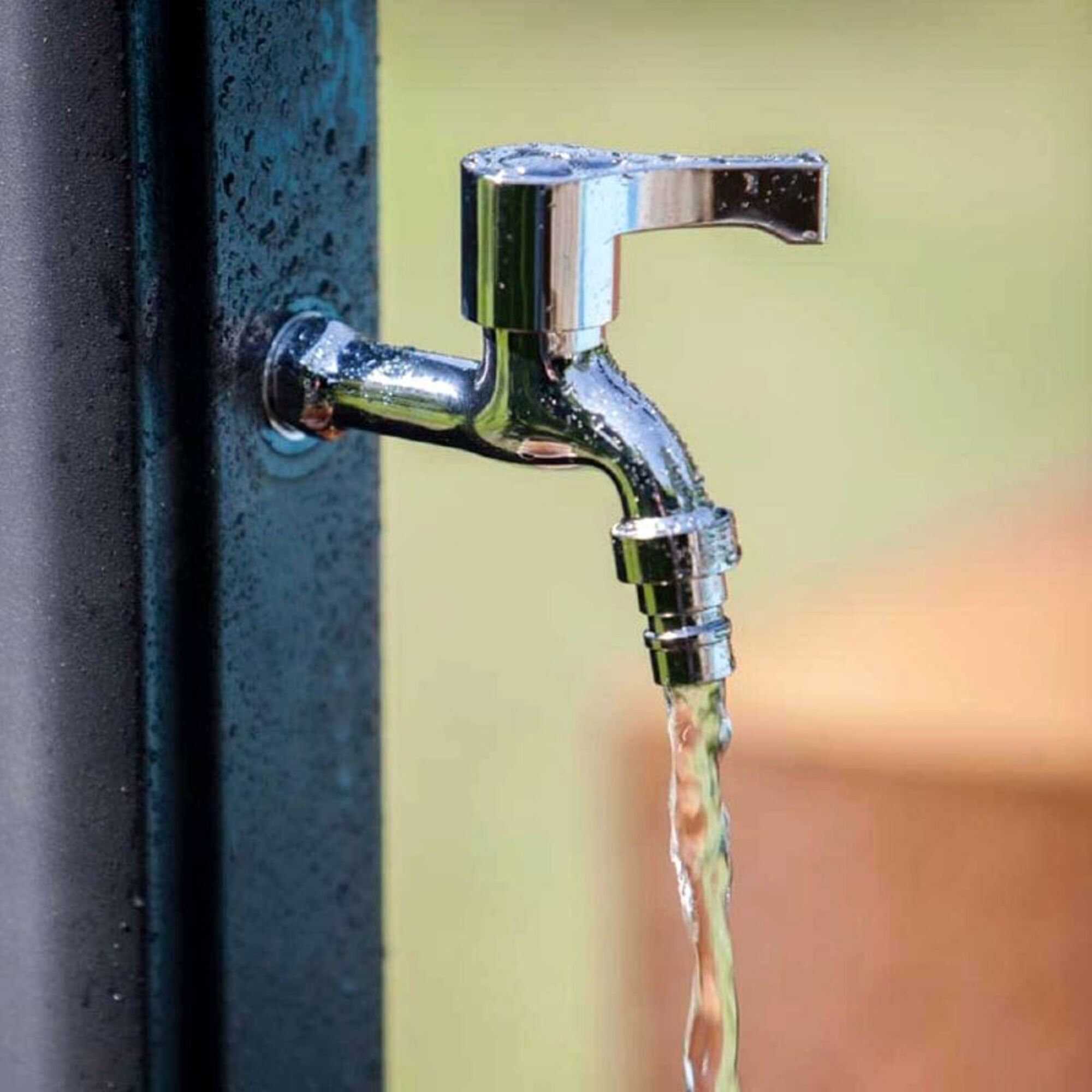 Un grifo plateado con agua corriendo, sobre un fondo borroso.