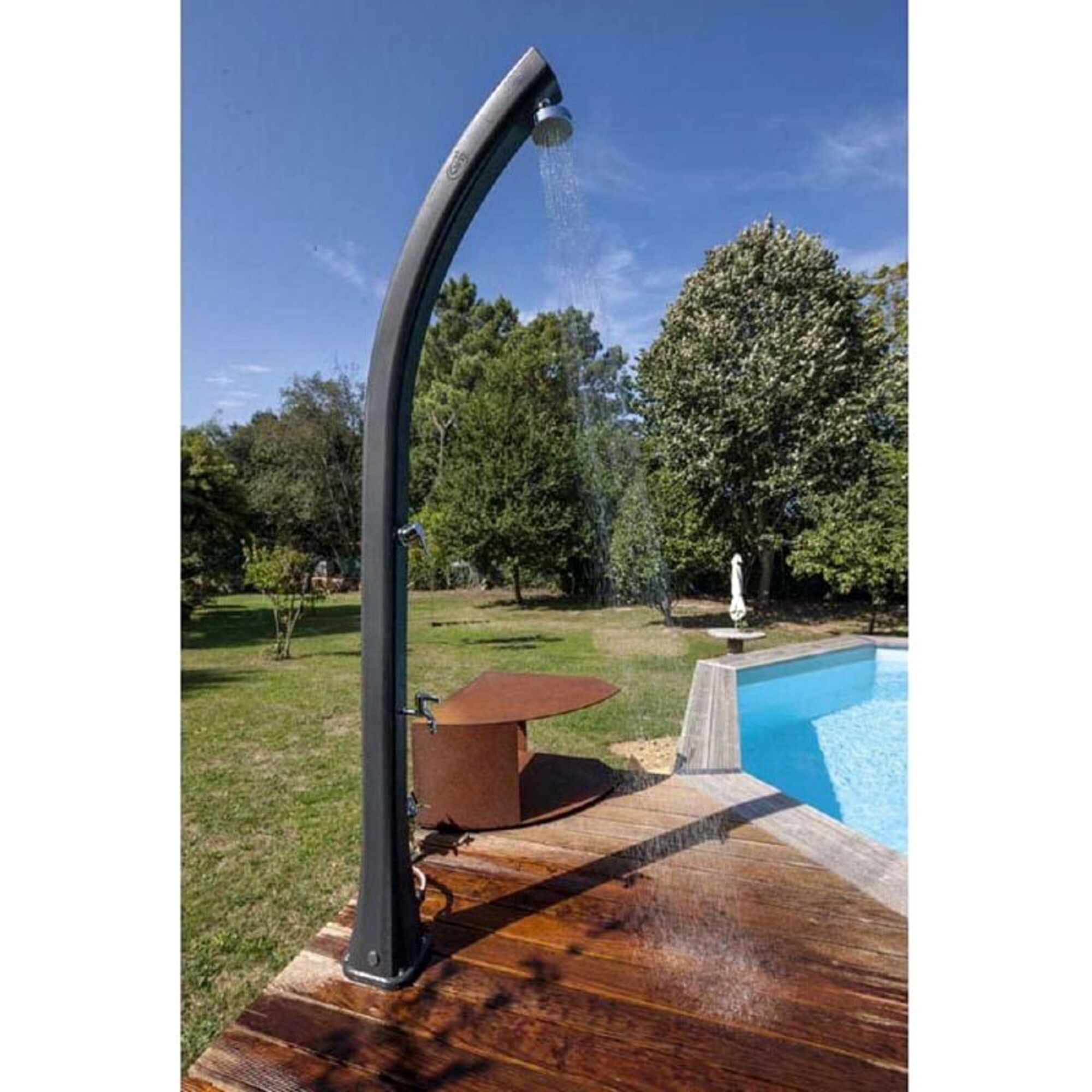 Ducha exterior junto a una piscina con agua fluyendo. Terraza de madera y árboles.