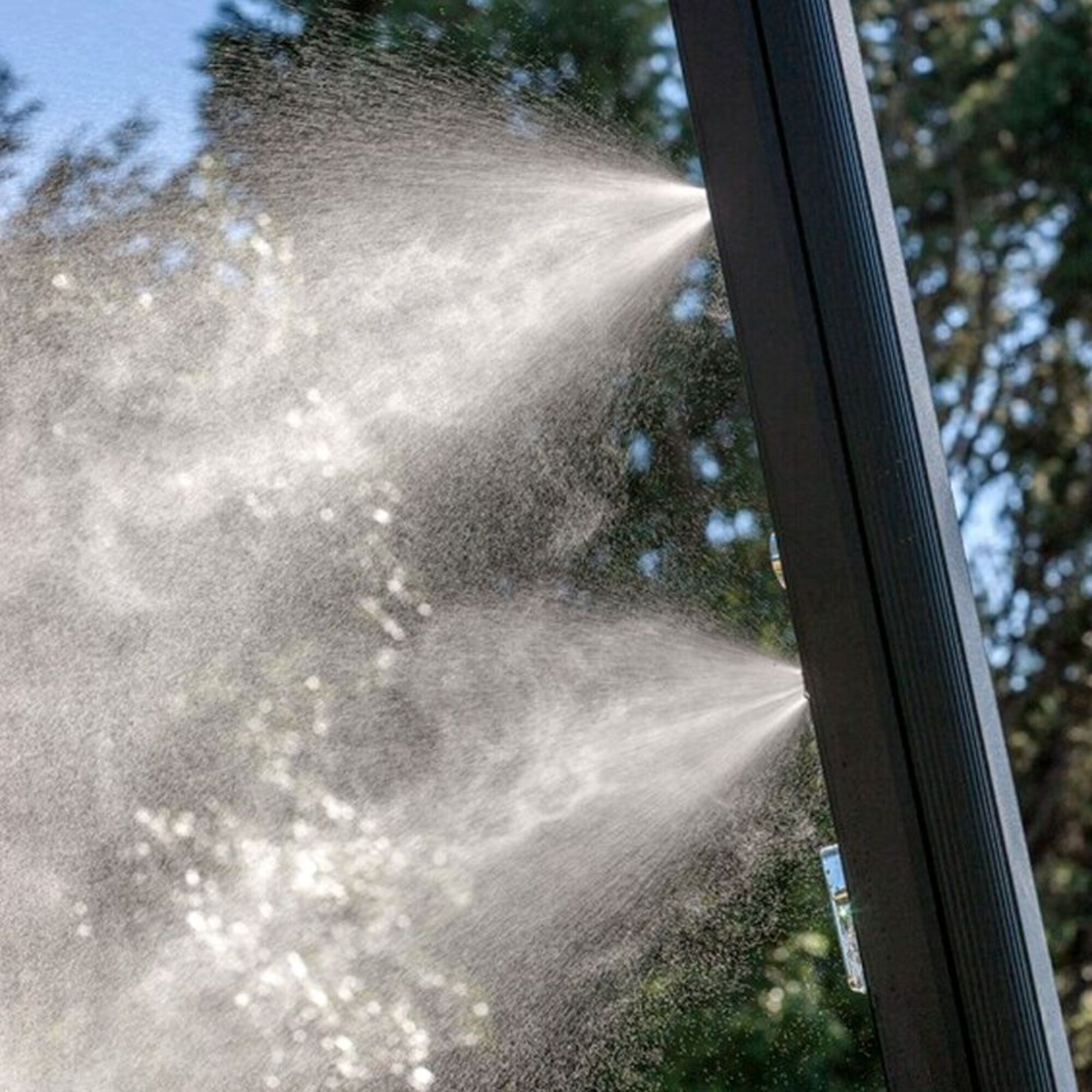 Un aspersor rocía finas gotas de agua contra un poste oscuro.