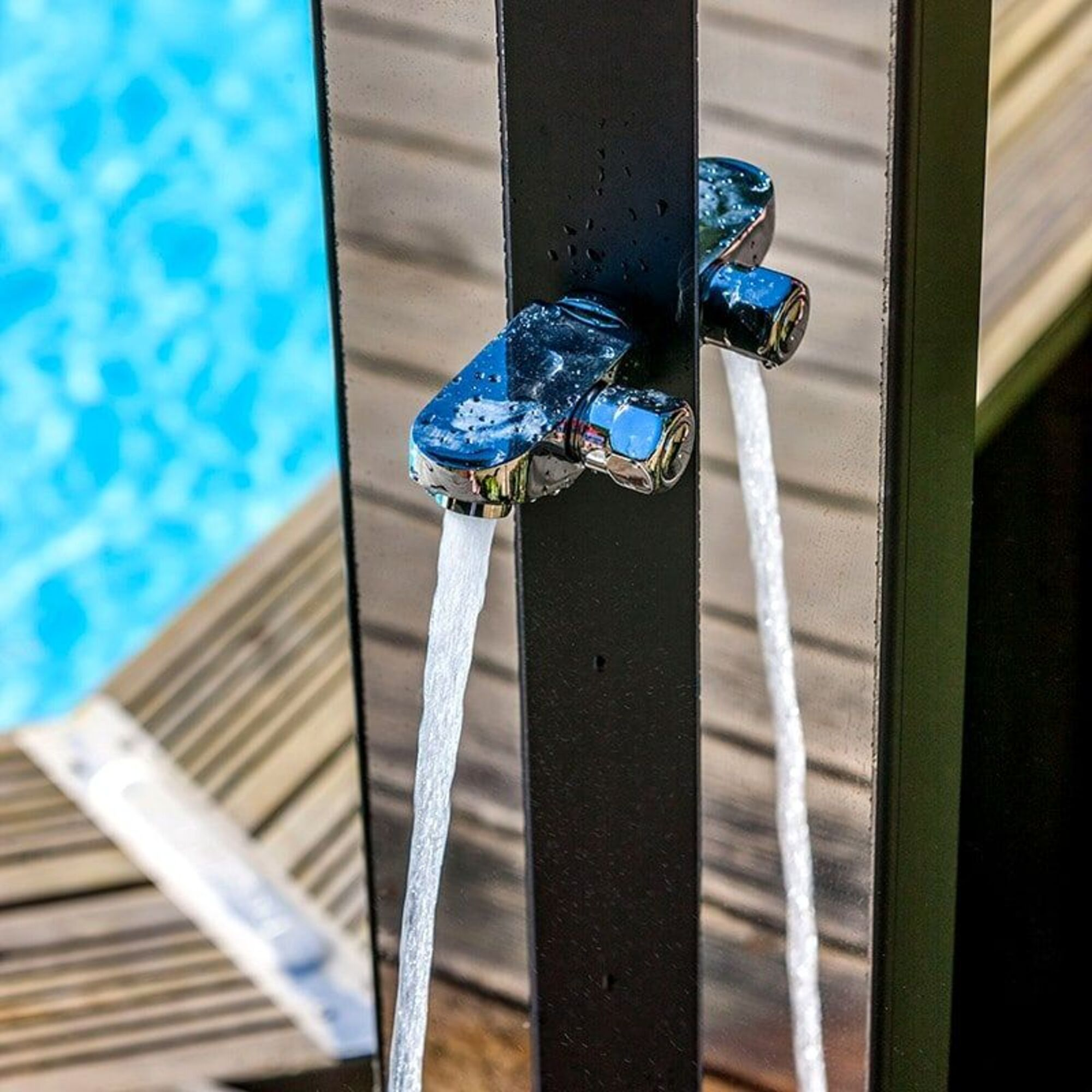 Un grifo de ducha con agua fluyendo junto a una piscina.