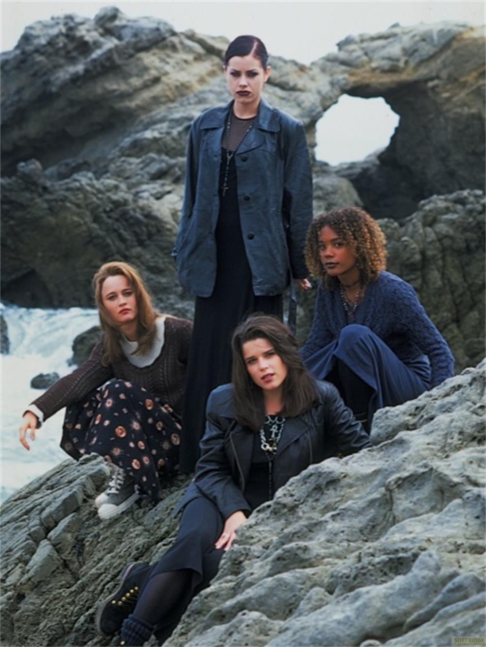 Quatre jeunes femmes posent sur un terrain rocheux près de la mer, avec des vagues.