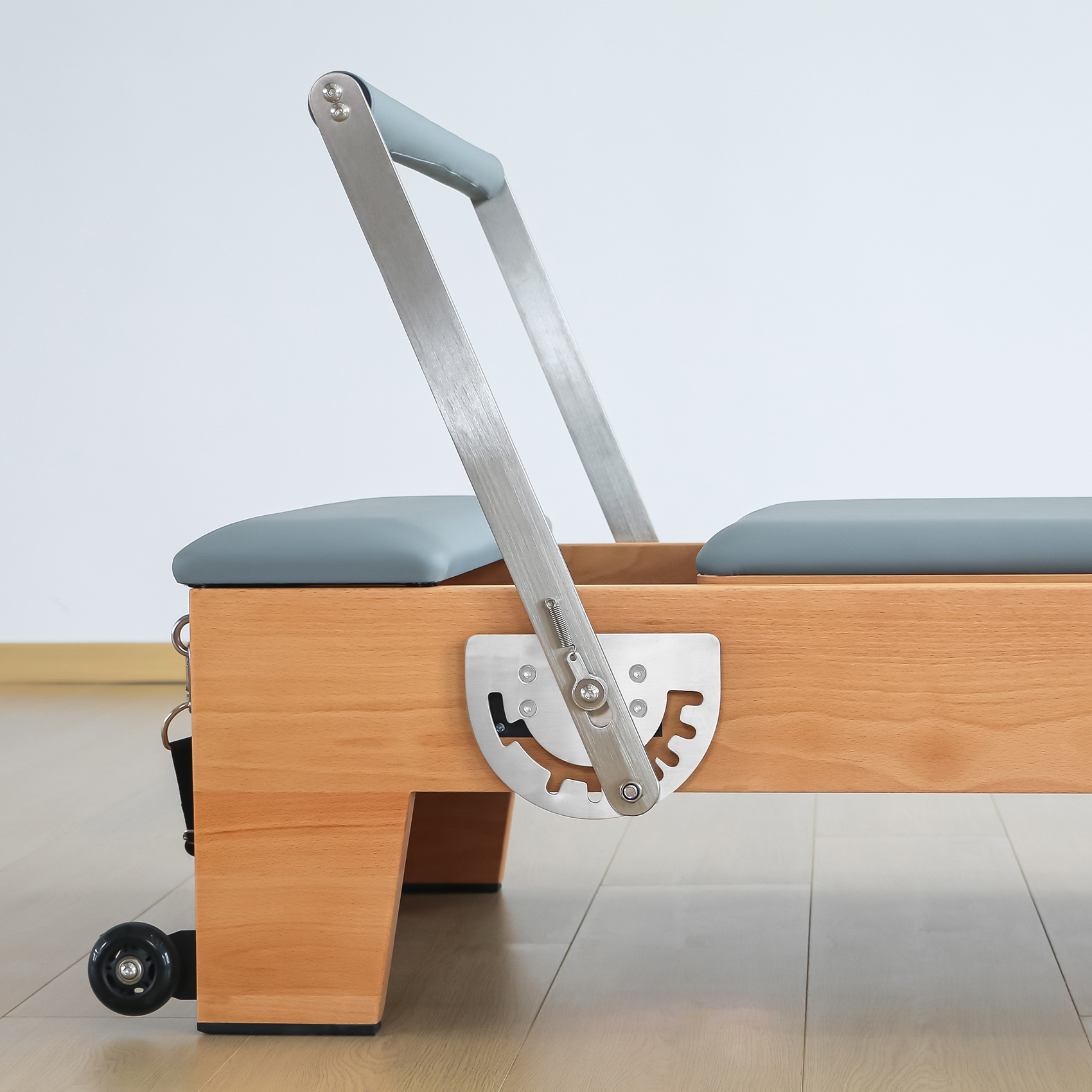 Pilates Reformer mit Holzrahmen, grauer Polsterung und Metallteilen.