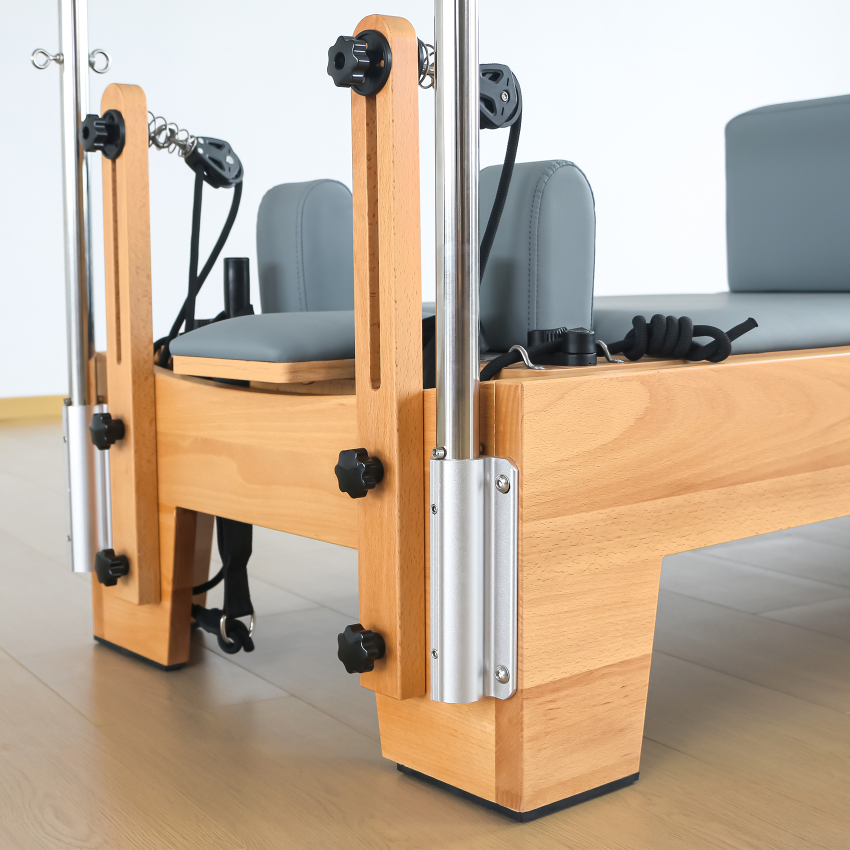 Ein hölzerner Pilates-Reformer mit grauen Polstern und schwarzen Seilen.