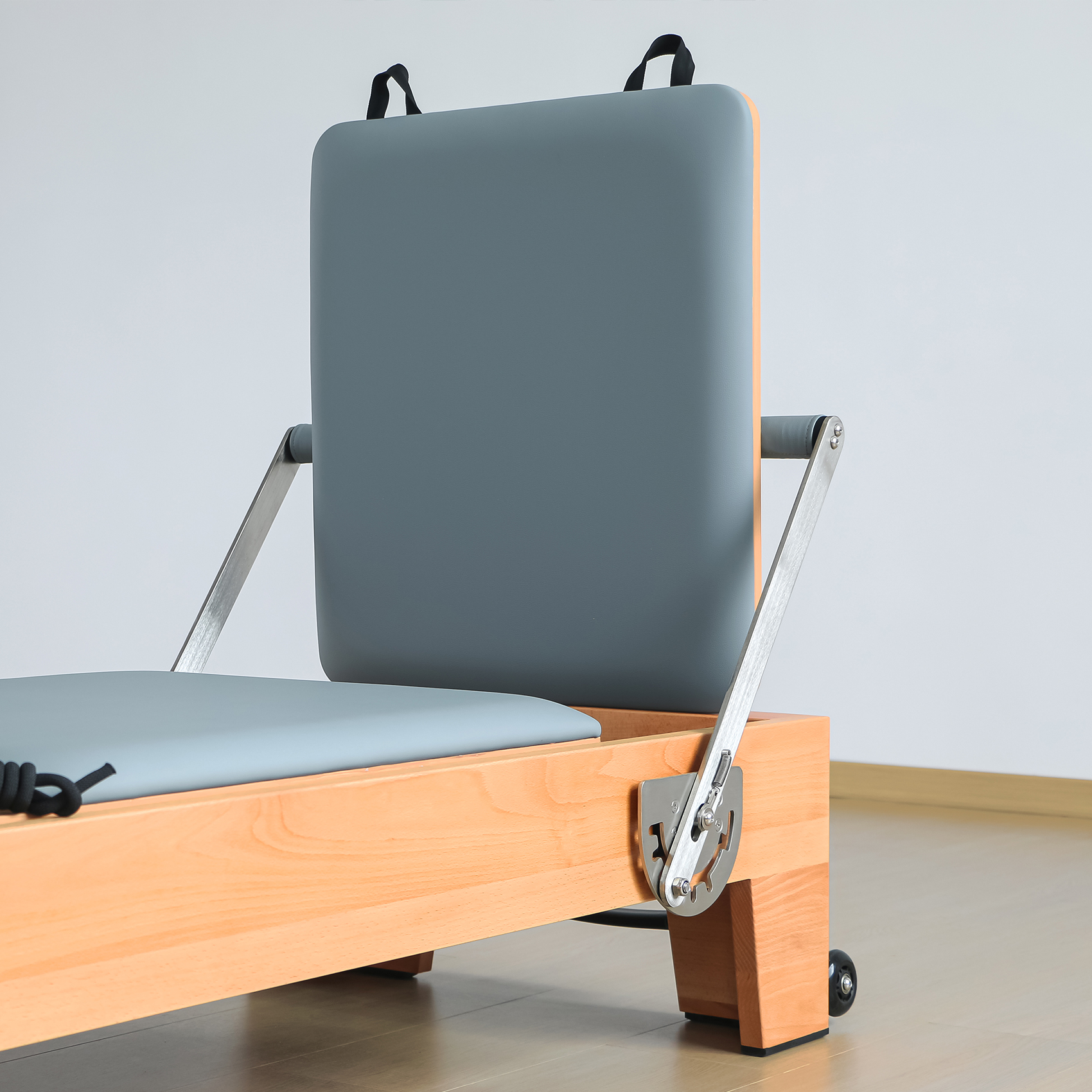 Ein Pilates-Reformer mit Holzrahmen, grauen Polstern und Metallteilen.