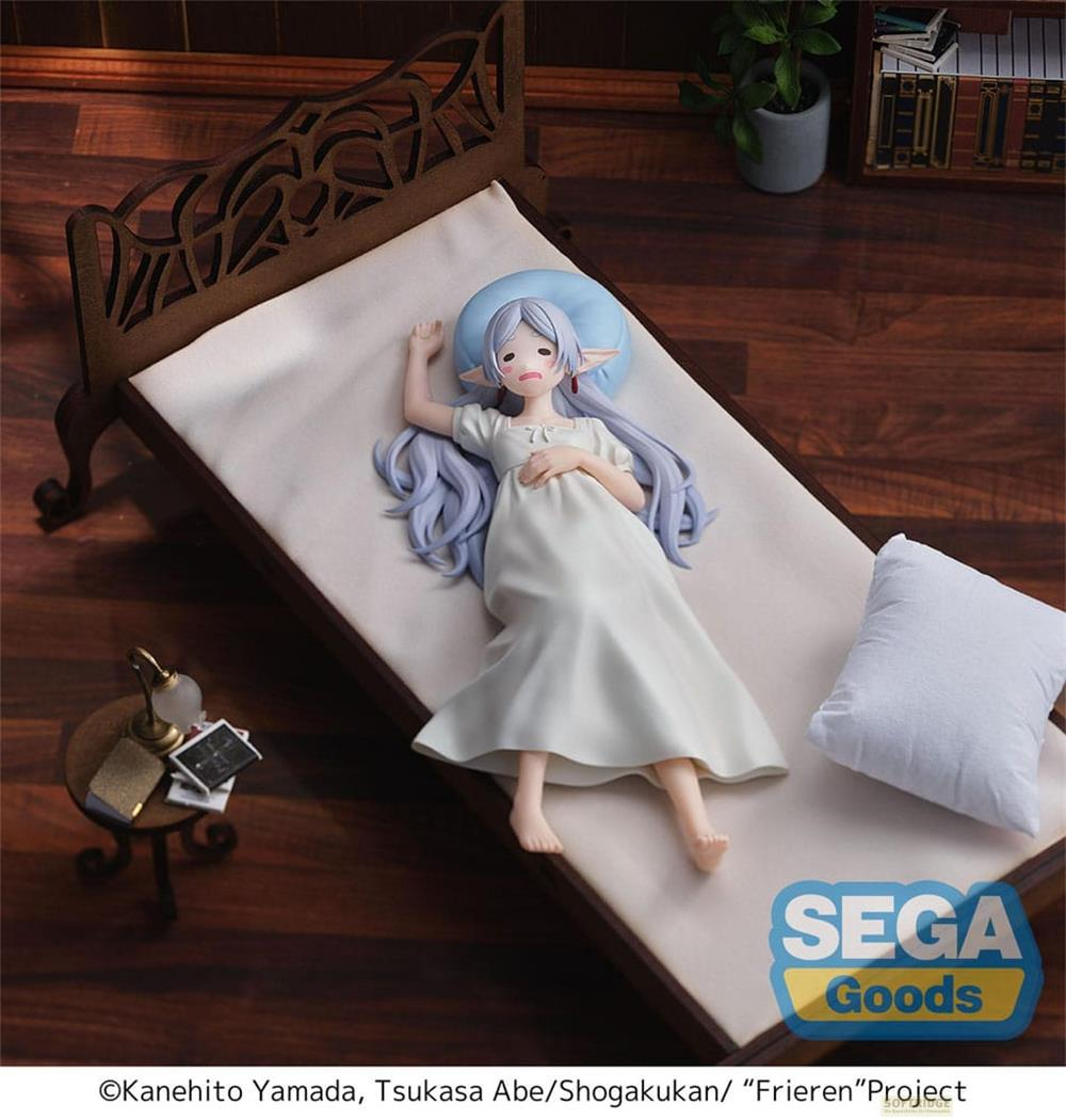 Eine Figur liegt in einem weißen Nachthemd auf einem Bett mit blauen Kissen.