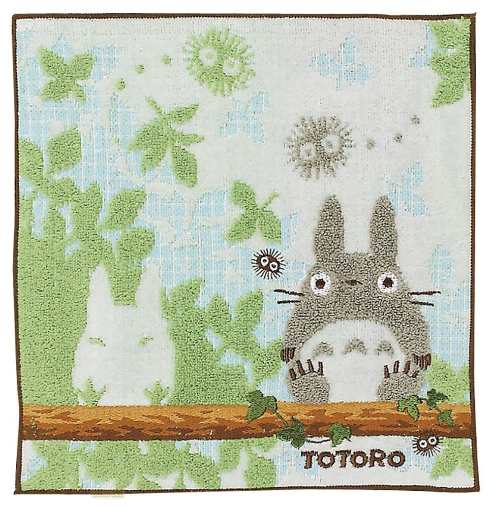 Totoro et un esprit blanc sont assis sur une branche devant des feuilles vertes.