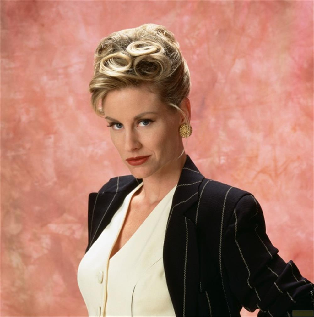 Donna con capelli biondi raccolti, in tailleur, su sfondo rosa.