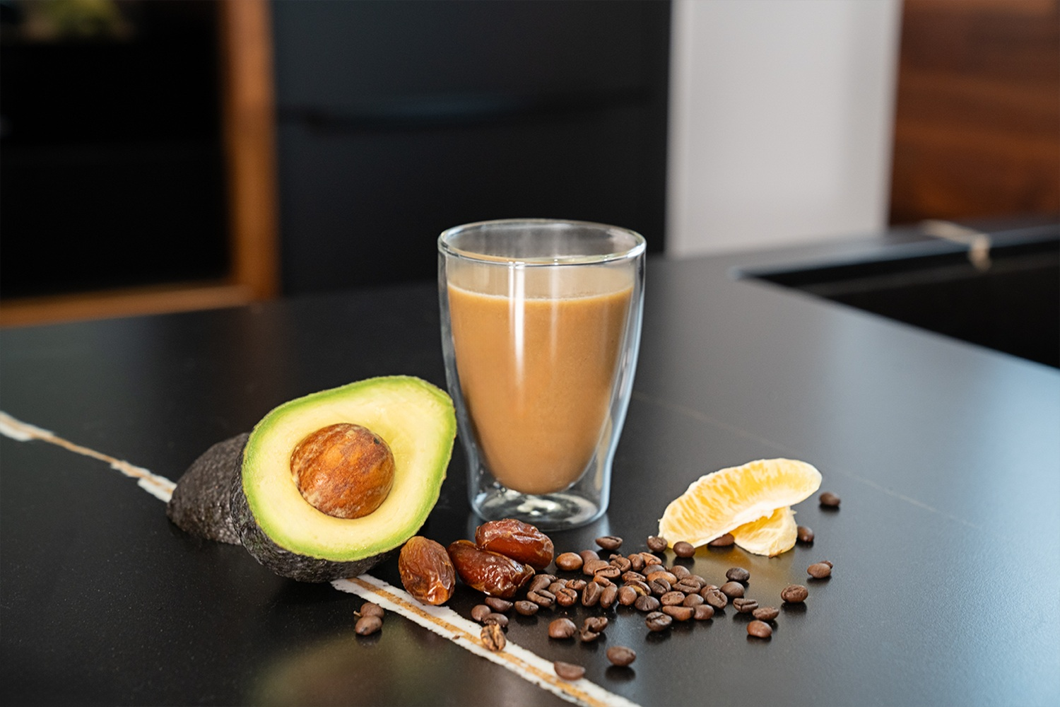 Ein Glas Kaffee neben Avocado, Datteln, Kaffeebohnen und Orangenscheiben.