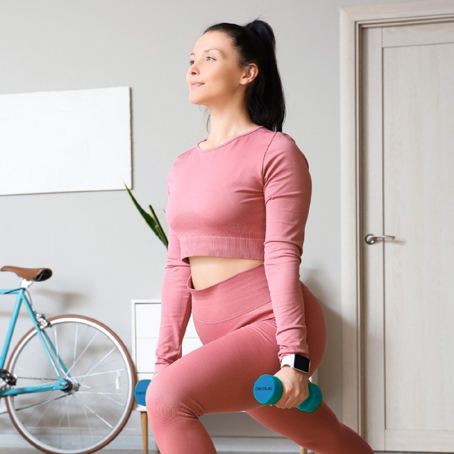 Donna in abiti sportivi rosa fa affondi con manubri blu.