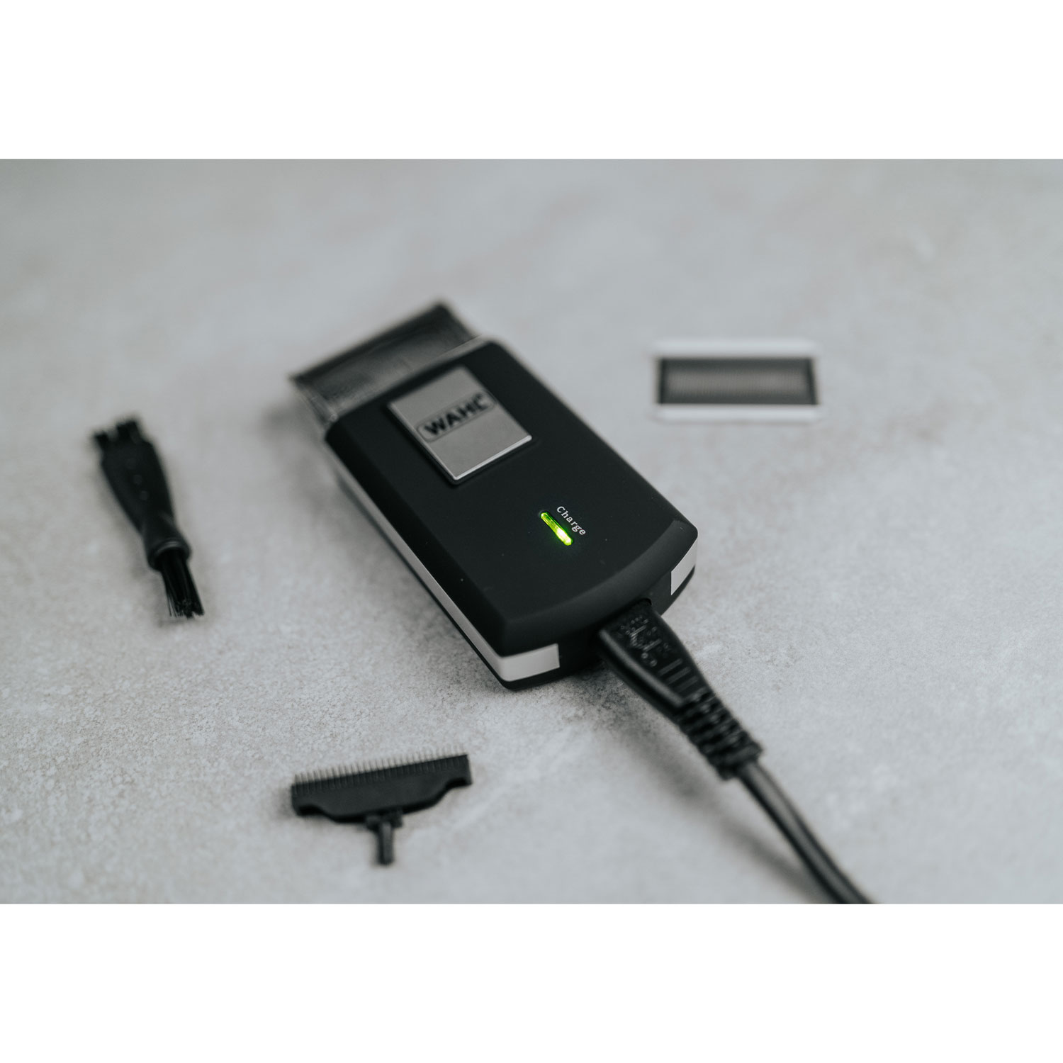 Czarna maszynka do strzyżenia Wahl ładuje się z akcesoriami na szarej powierzchni.