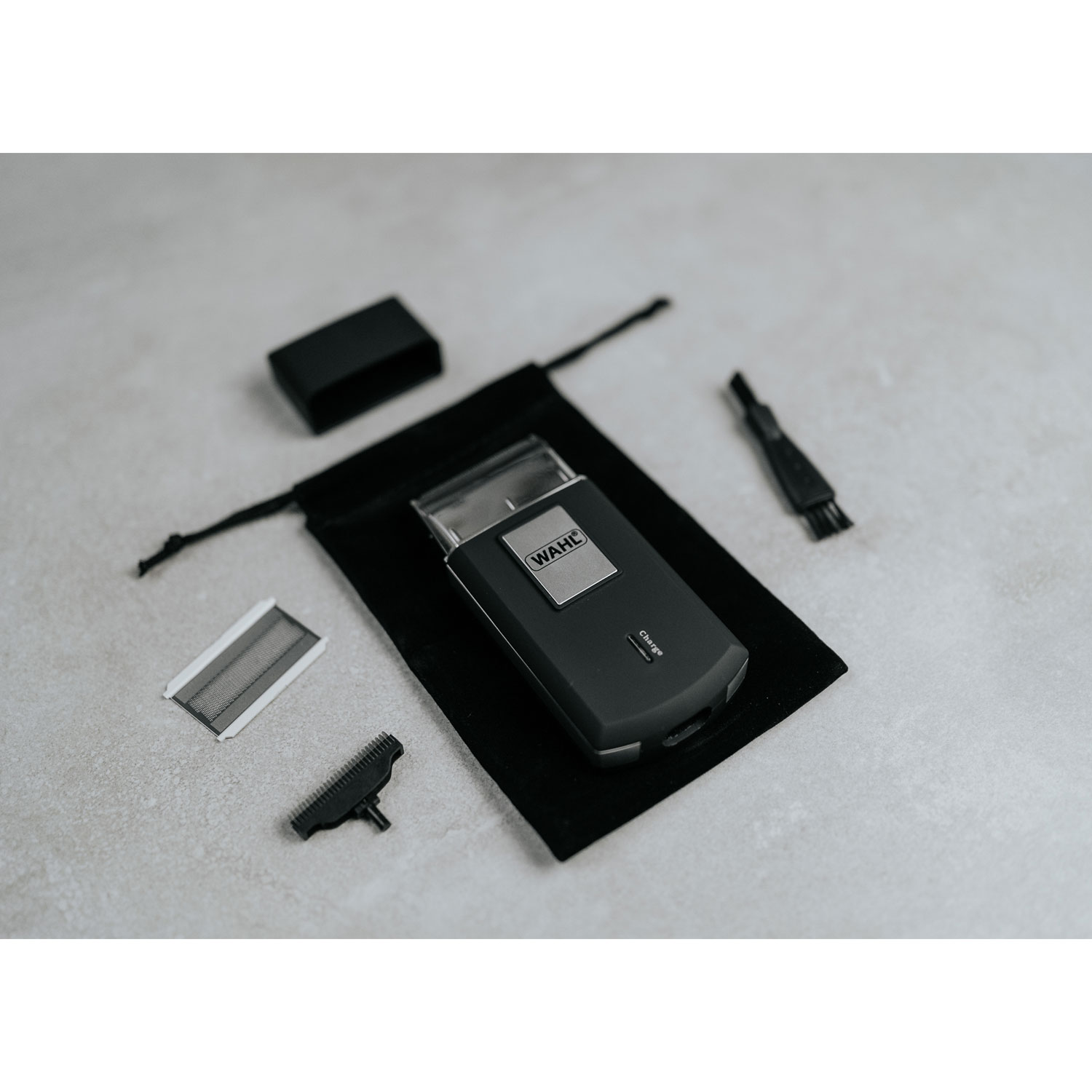 Golarka Wahl, kabel do ładowania, szczoteczka, folia i nakrętka na szarej powierzchni.