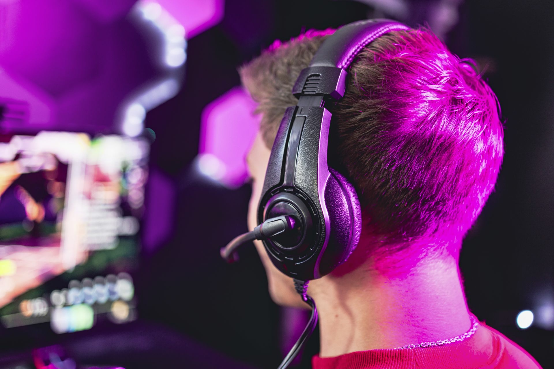A person wearing headphones looks at a blurred screen, lit by pink light.