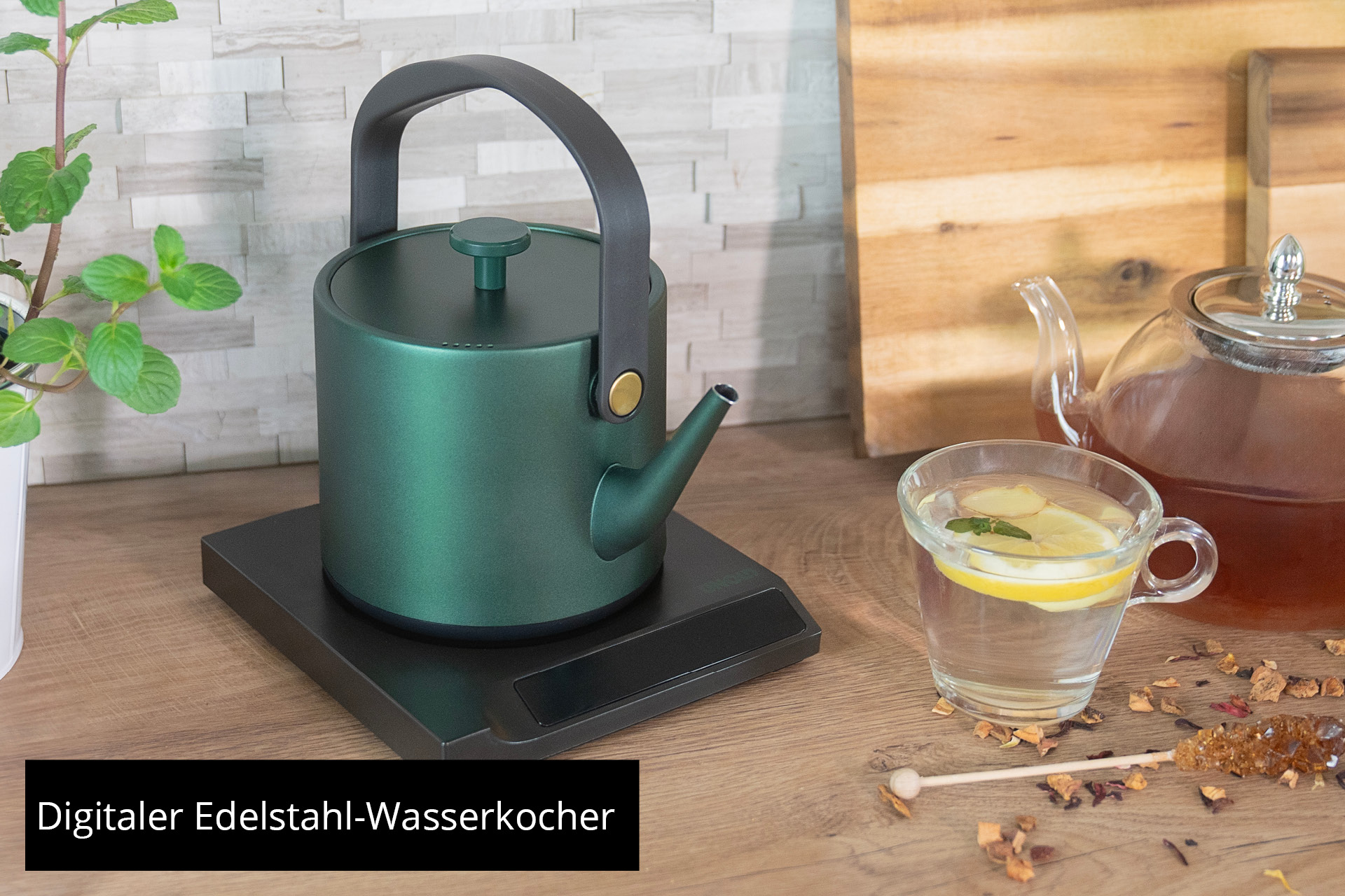 Bouilloire verte sur socle, à côté un verre de thé au citron et à la menthe.