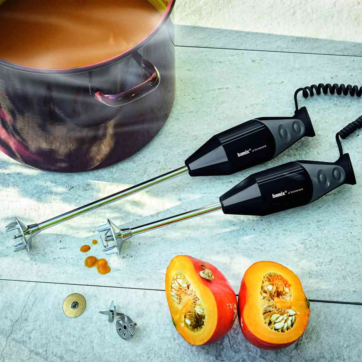Due frullatori a immersione accanto a una pentola e una zucca dimezzata.