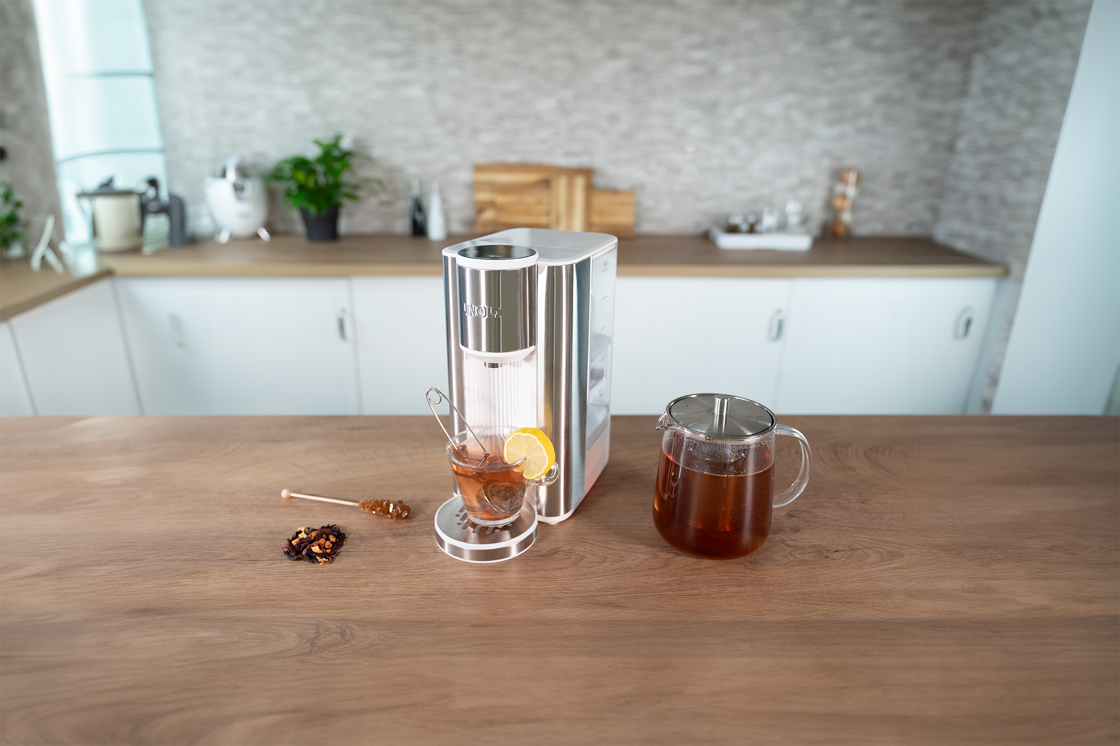 Ein silberner Wasserspender mit einer Tasse Tee und einer Teekanne auf einem Holztisch.