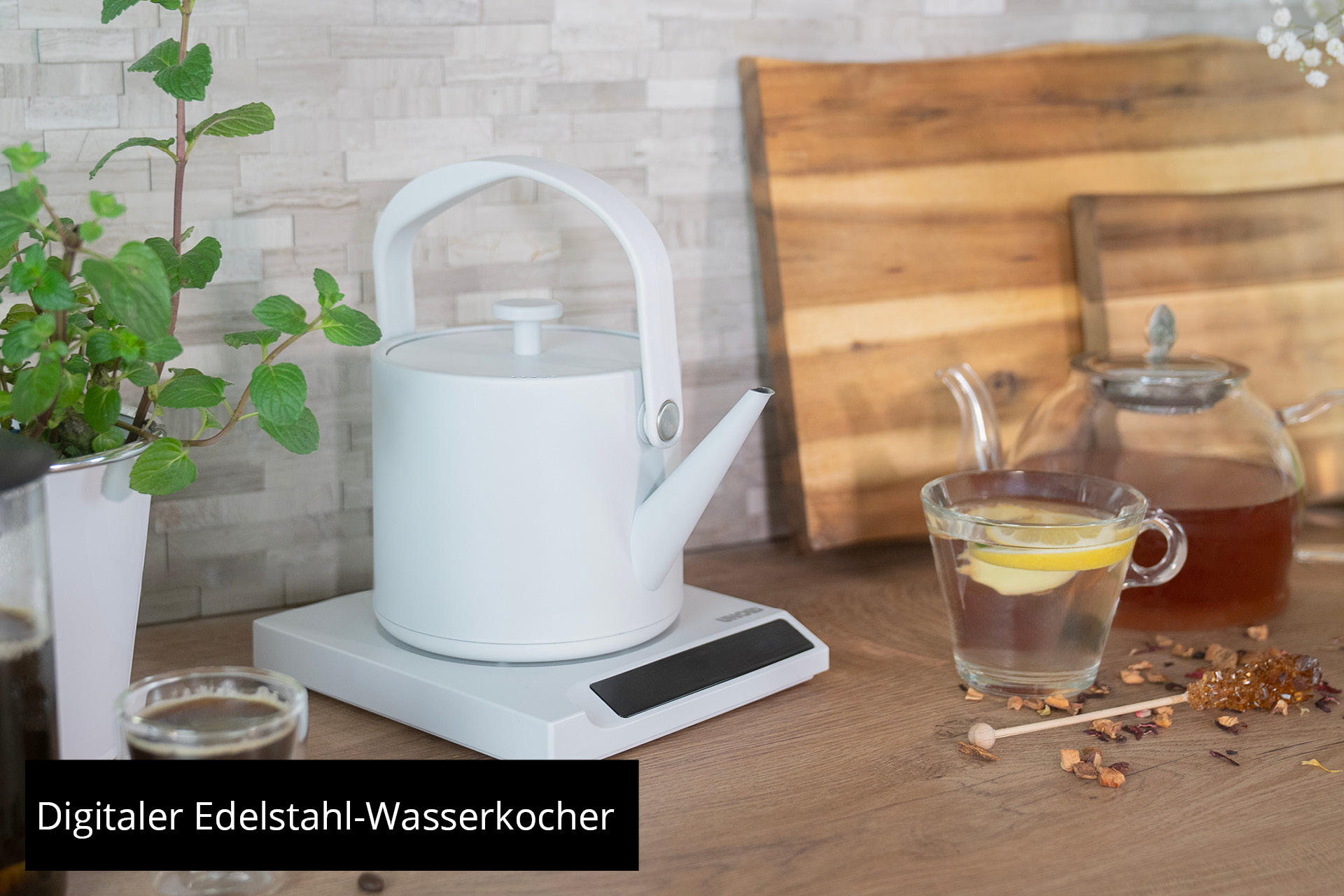 Eine weiße Teekanne auf einer digitalen Waage, daneben eine Tasse Tee.