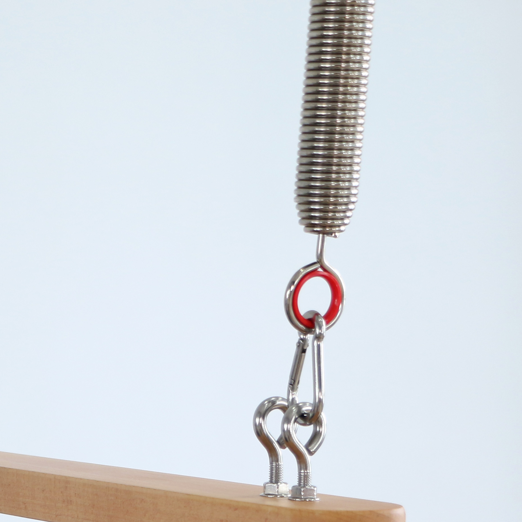 Metallfeder mit rotem Ring und Karabinerhaken, die an einem Holzbrett befestigt sind.