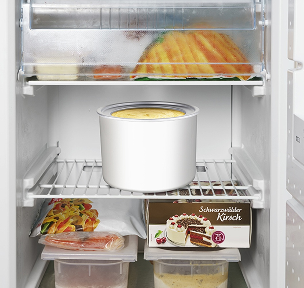 Biała maszynka do lodów stoi na półce w otwartej lodówce.