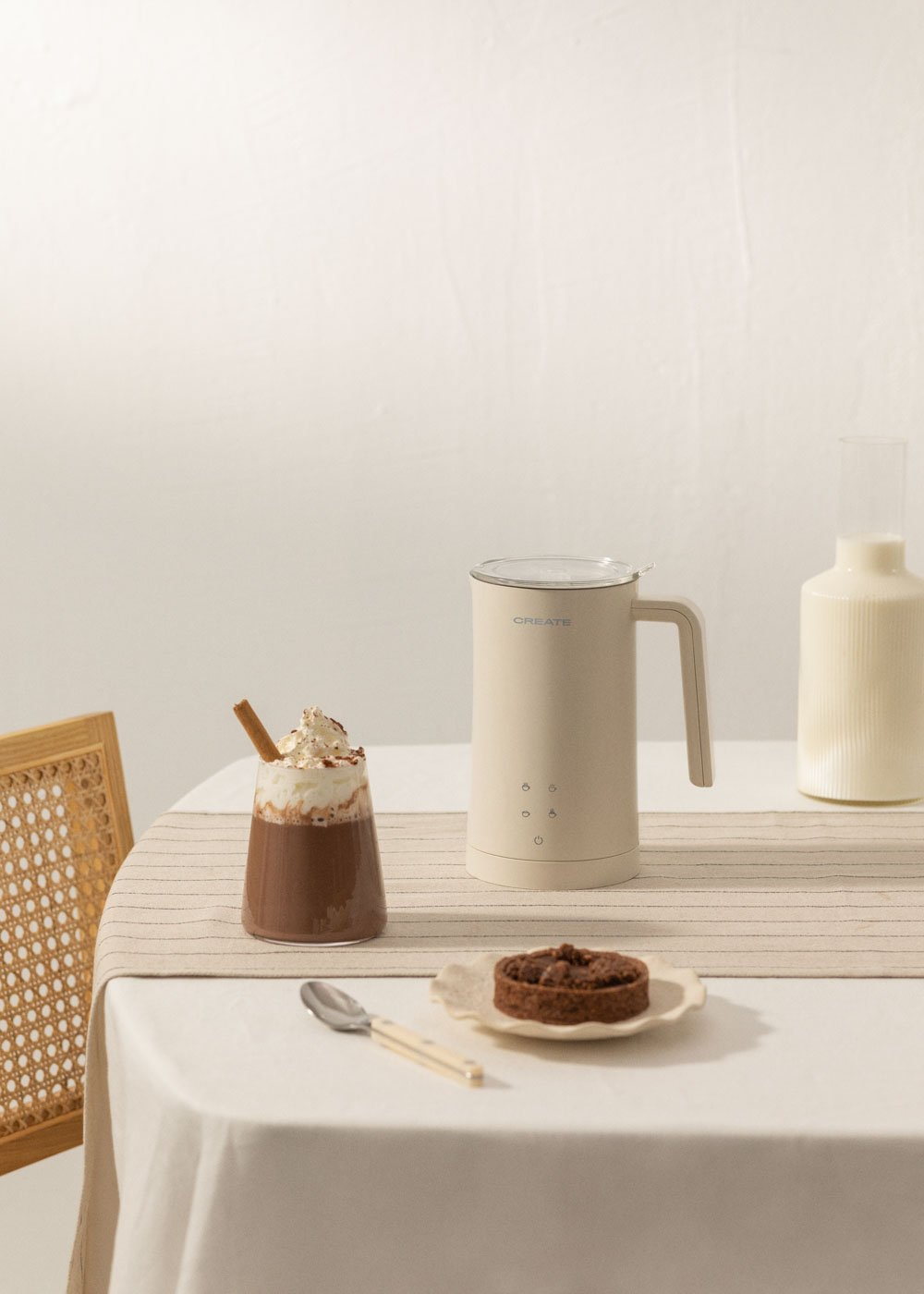 Una bebida de chocolate con nata, un espumador de leche y un pastel en una mesa.