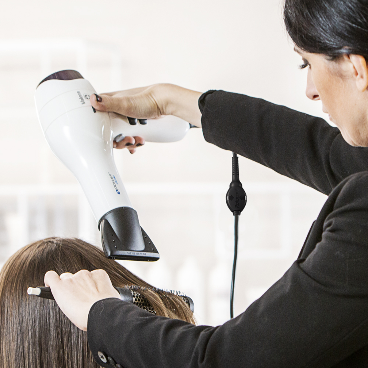 Osoba suszy włosy innej osobie białym suszarką.