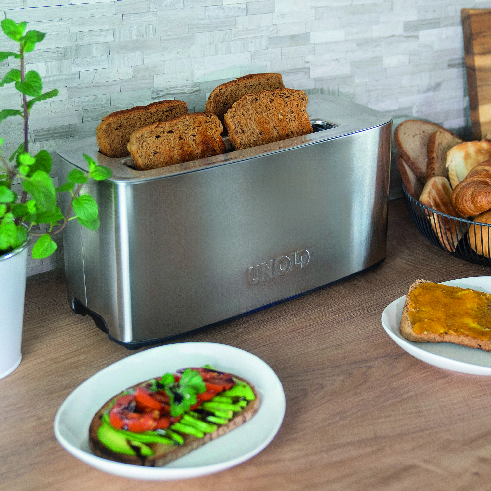 Ein silberner Toaster mit Toast, daneben Brot und Gebäck in einem Korb.