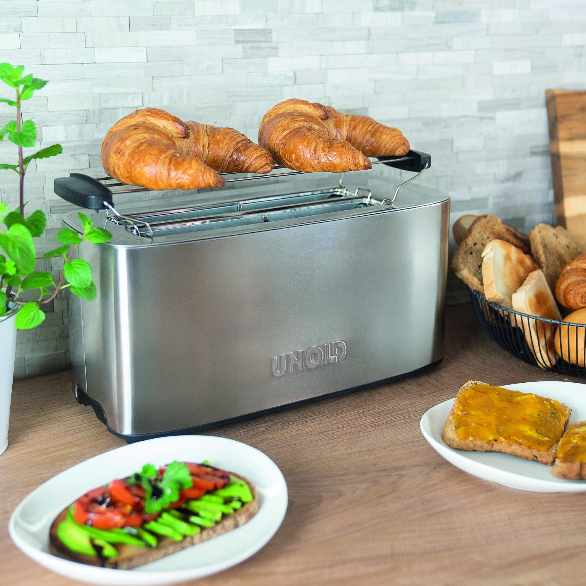 Ein silberner Toaster mit Croissants darauf. Avocado-Toast und Marmeladen-Toast daneben.