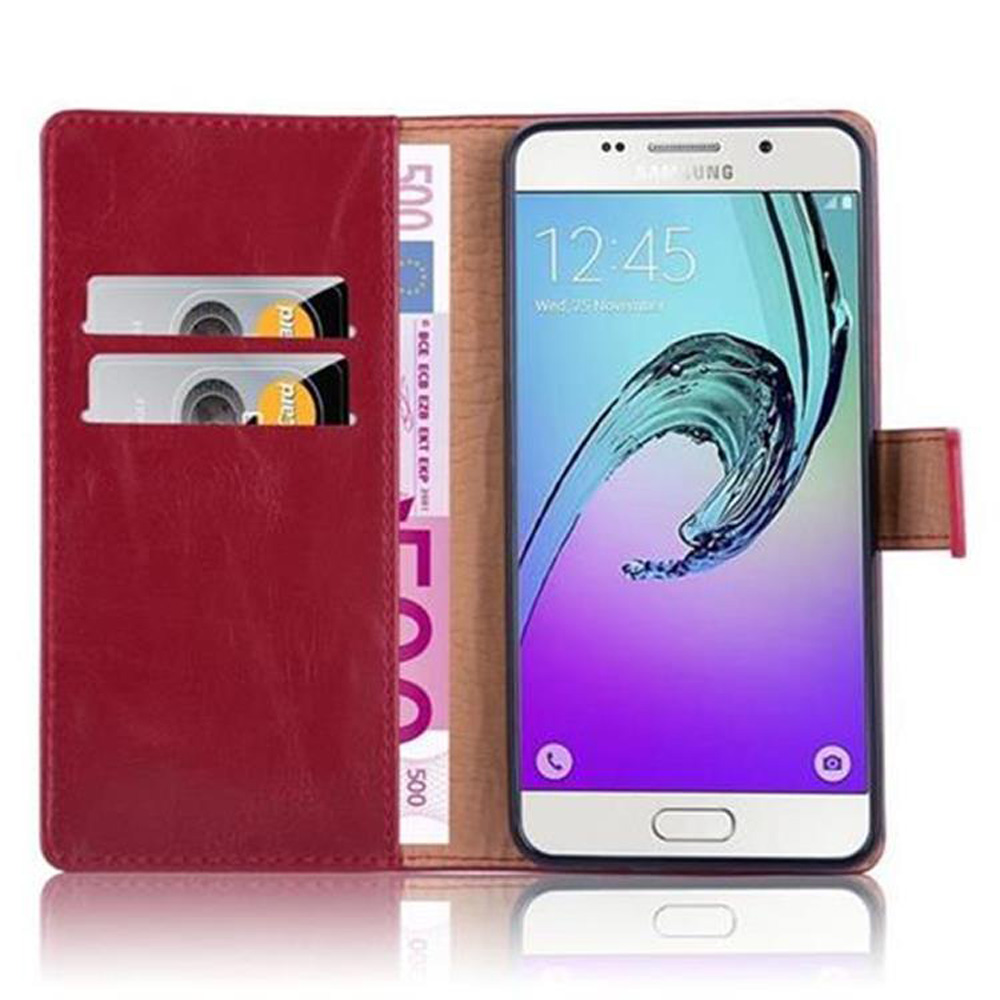 Una custodia a portafoglio in pelle rossa mostra carte e banconote da 500 euro. Accanto uno smartphone.